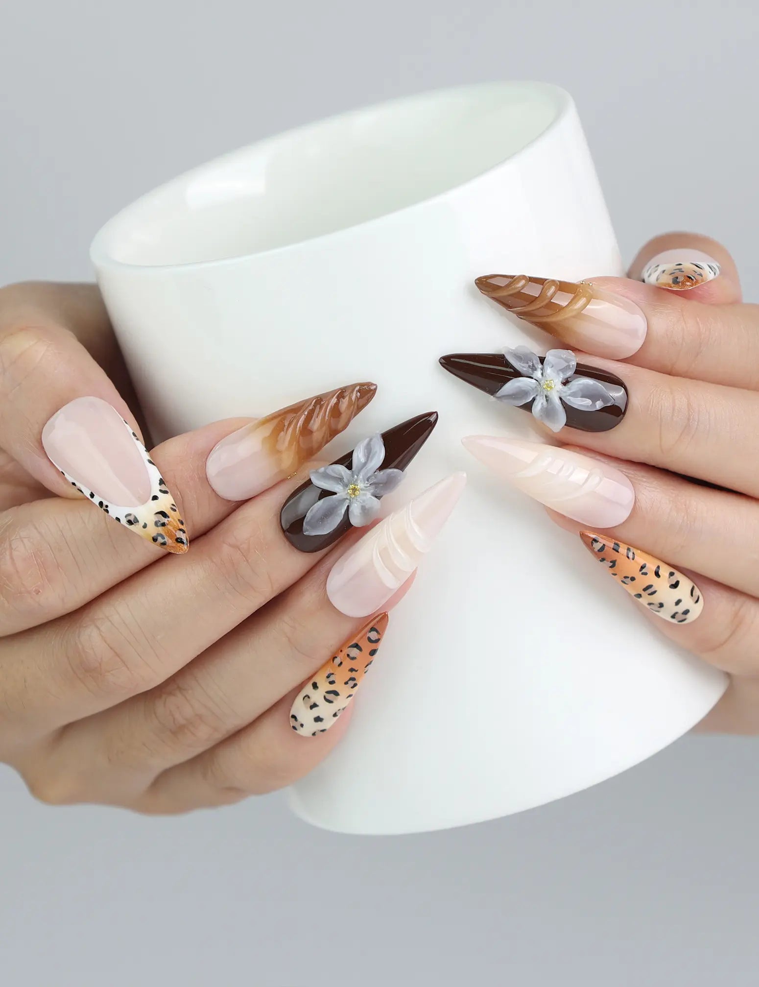 Hand holding a cup, wearing Naillover leopard and black press-on nails with feminine flower accents for contrast