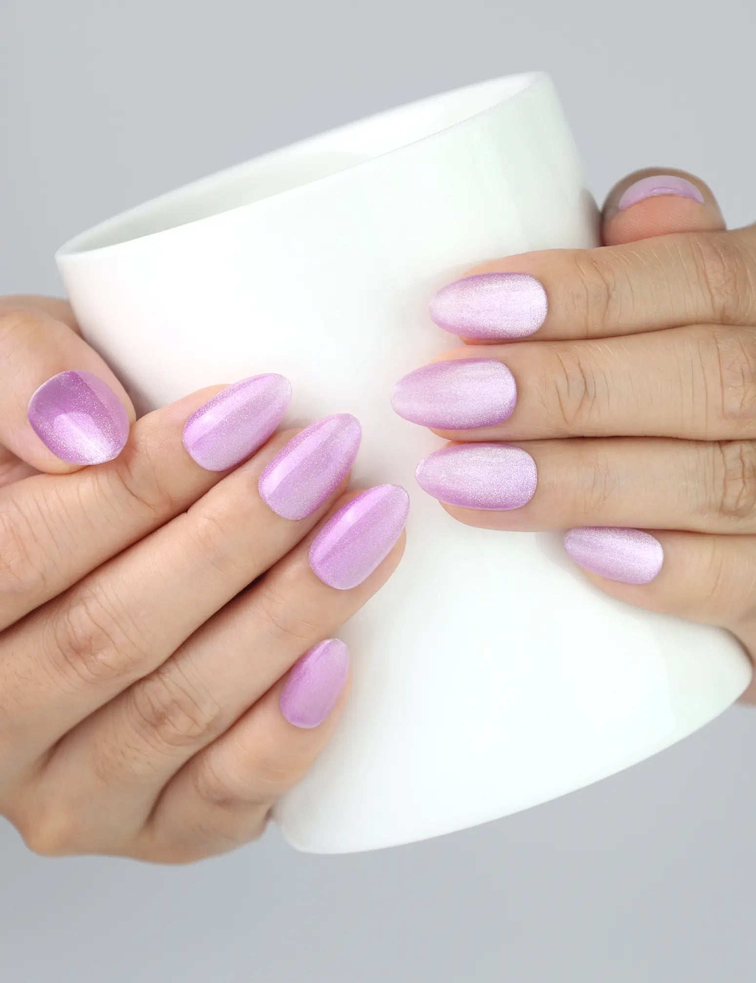 Hand holding a ceramic cup, featuring Naillover’s Lilac Sparkle press on nails in soft purple cat eye style.