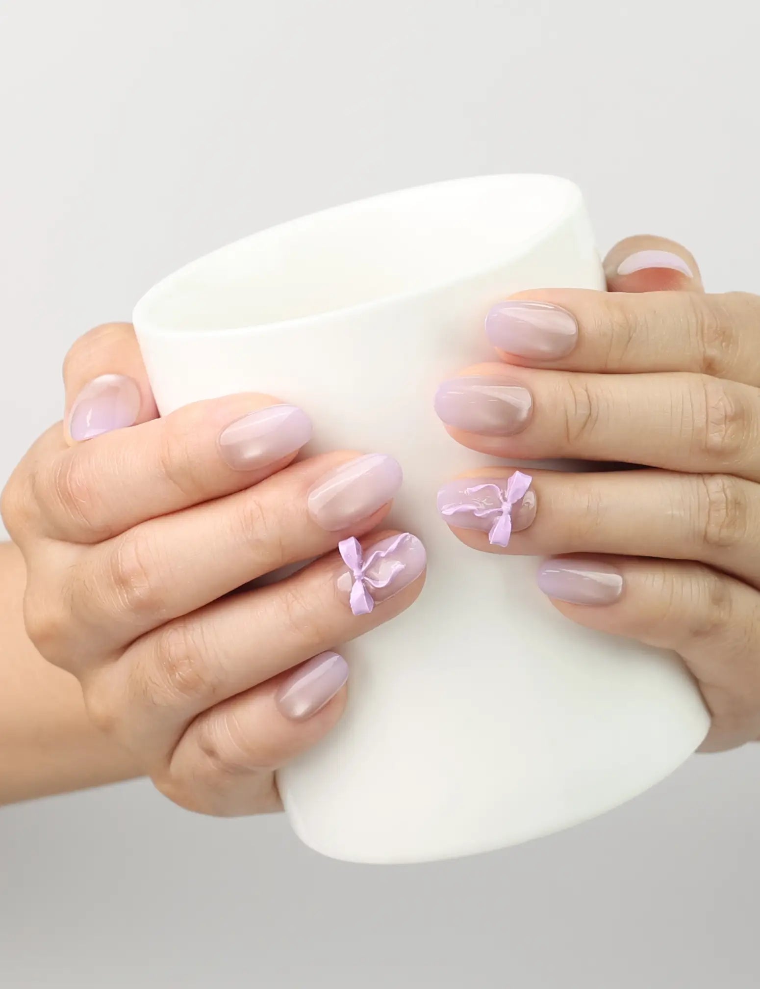 Naillover Lilac Whisper Singapore press on nails holding a teacup, showing beige base and lavender ribbon details