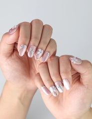 Close-up of hands showcasing pink press on nails featuring elegant floral patterns and shiny rhinestone embellishments by Naillover