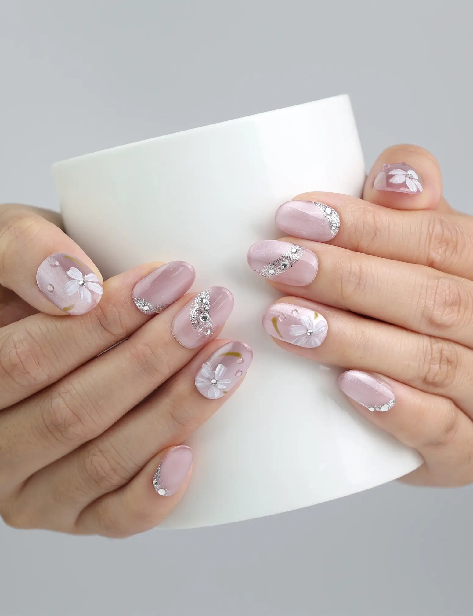 Hand holding a cup while wearing Singapore handmade pink nails with soft floral details and rhinestones by Naillover