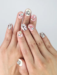 Hand model showing short silver-pink press-on nails with 3D hearts, pastel stars, and colorful gem decorations