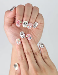 Hand model showing short silver-pink press-on nails with 3D hearts, pastel stars, and colorful gem decorations