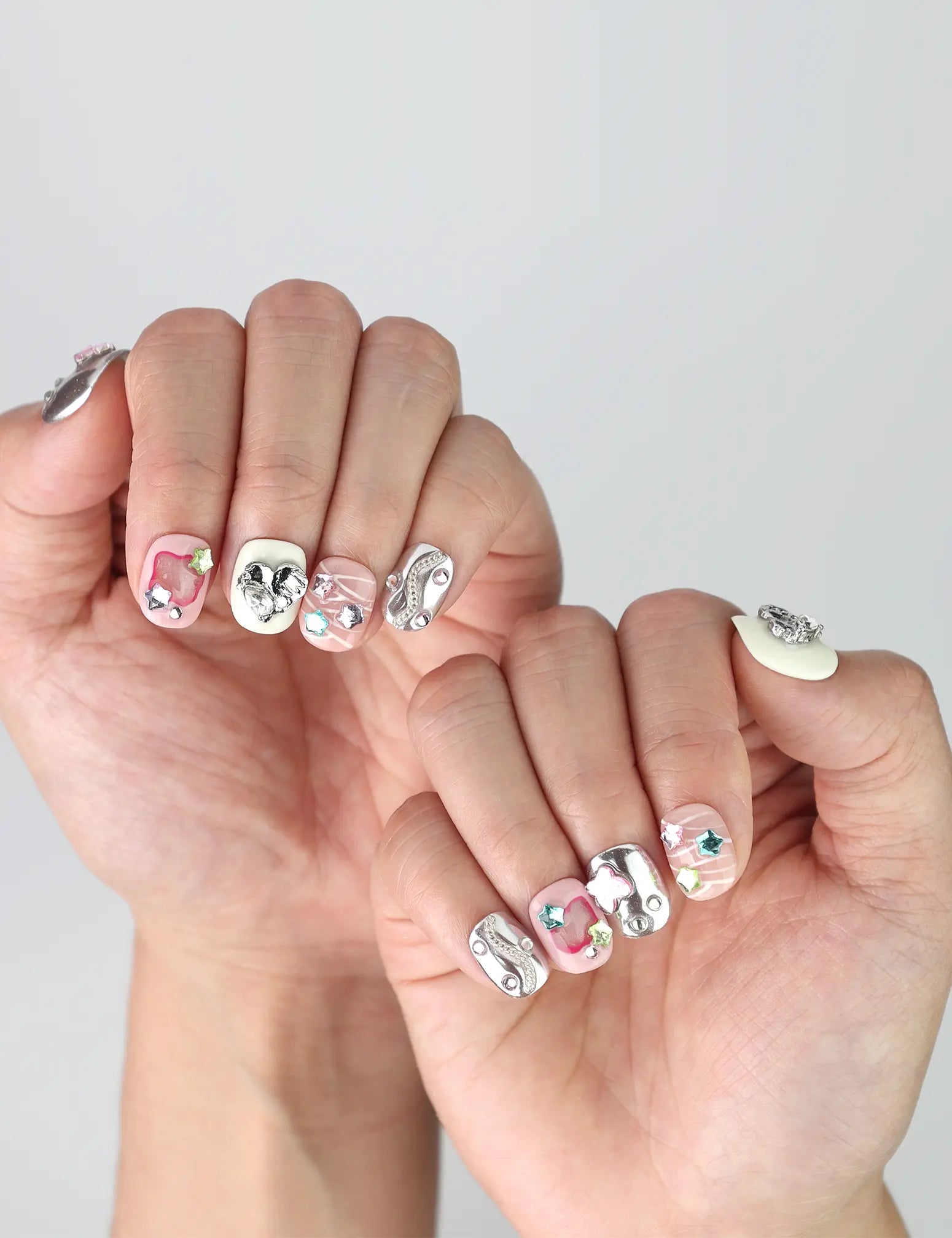 Side angle of short square press-on nails featuring soft chrome pink tones and raised 3D heart and star nail art