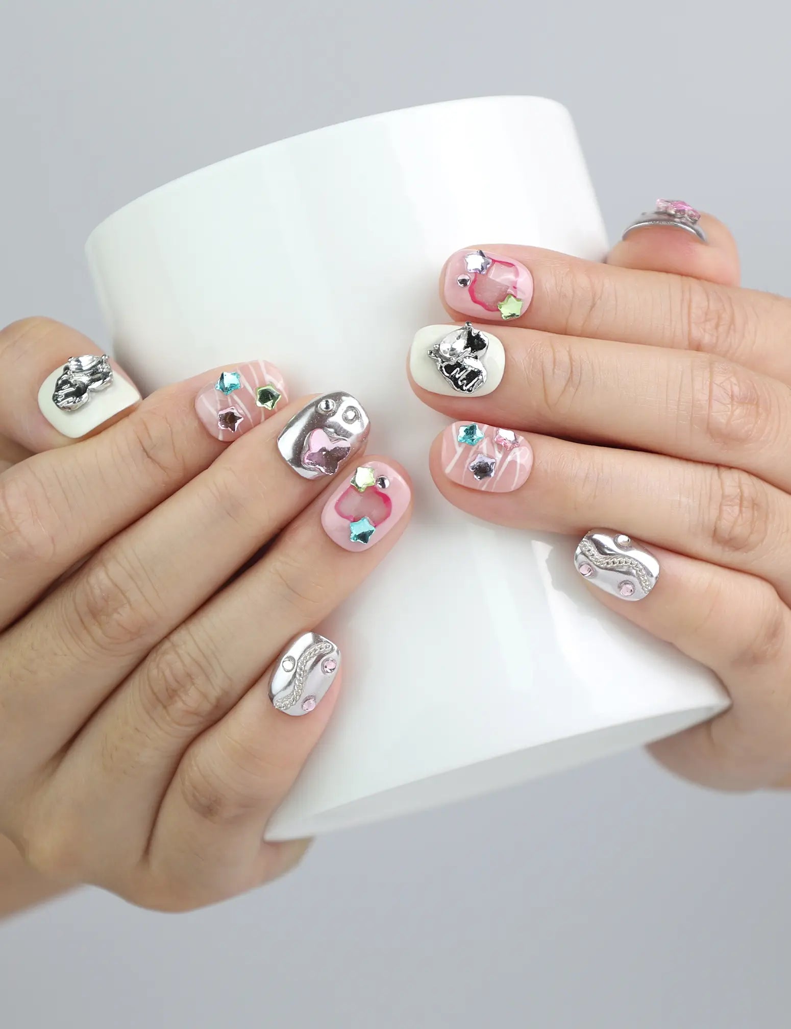 Hand holding a cup while wearing Naillover’s silver-pink short press-on nails with bold, colorful 3D gem details