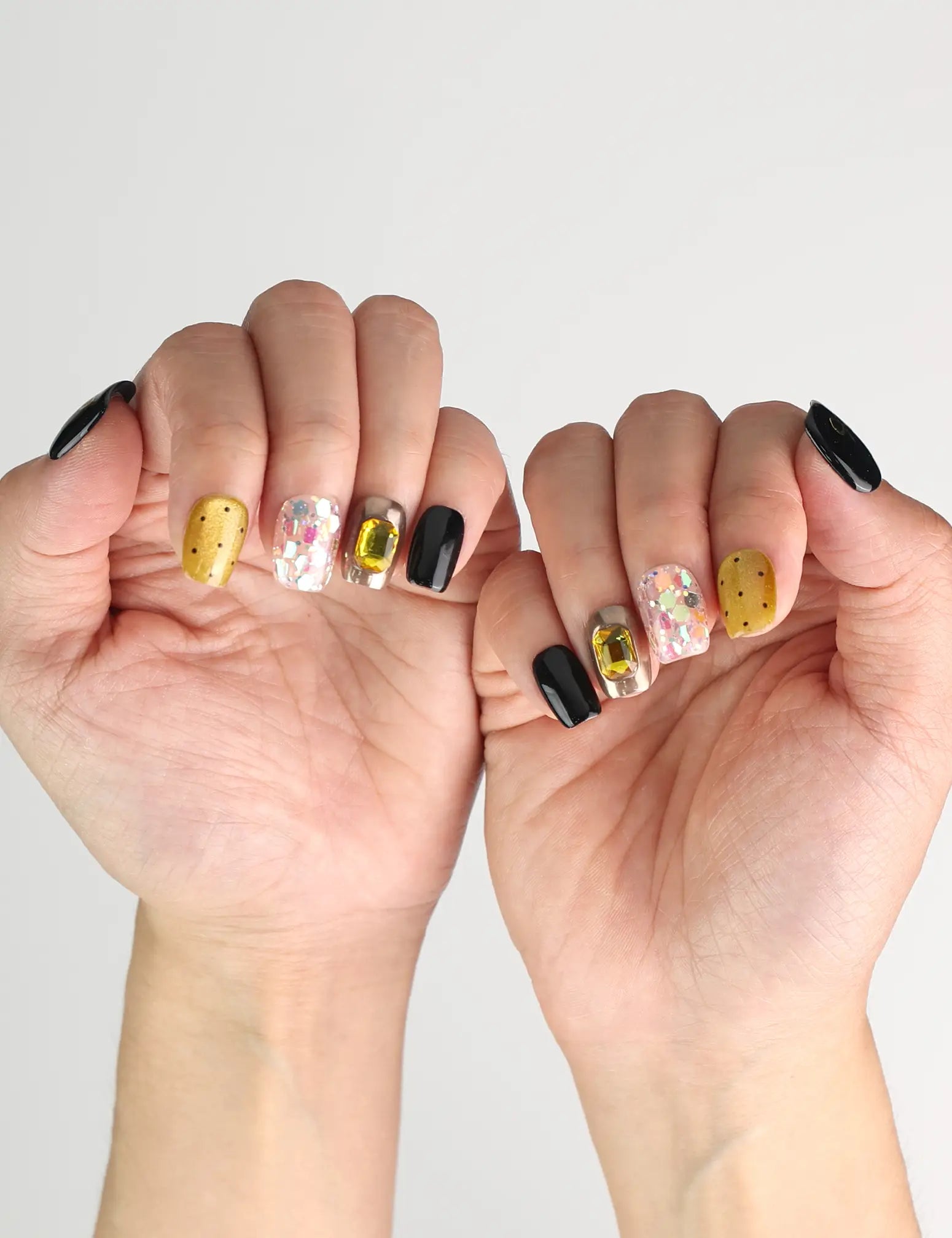 Side angle view of hand wearing Luxe Mix black, gold, glitter Singapore press on nails with gem accents, naillover