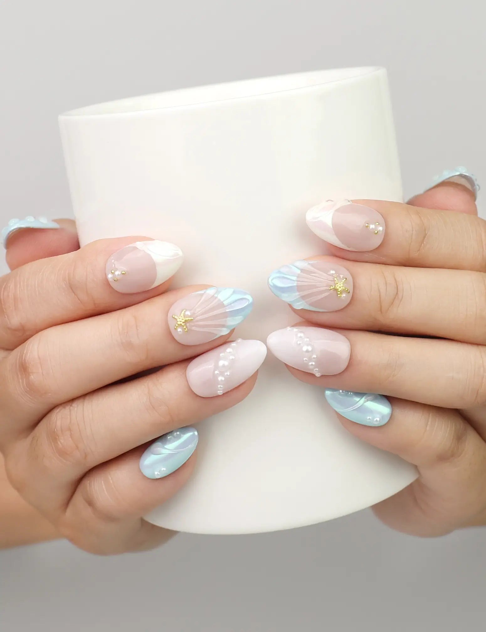 Hand holding a cup while wearing Naillover Marine Dream handmade press on nails with pastel shimmer and gold decorative accents.