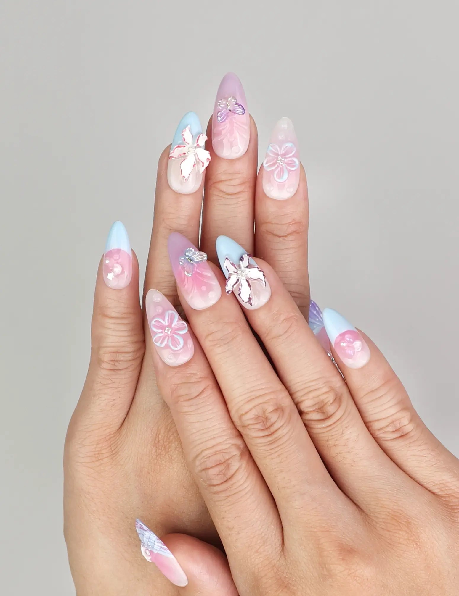 Hand model wearing Naillover Mermaid’s Floral Dream handmade press on nails in pink and blue with 3D floral accents, trendy nails Singapore.