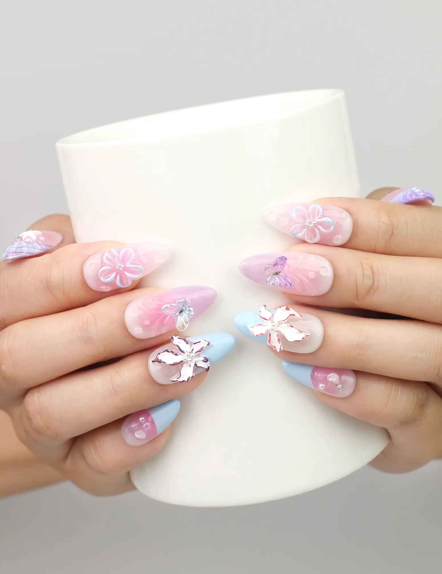 Hand holding a cup while wearing Mermaid’s Floral Dream handmade press on nails in pink and blue with 3D floral and butterfly charm.