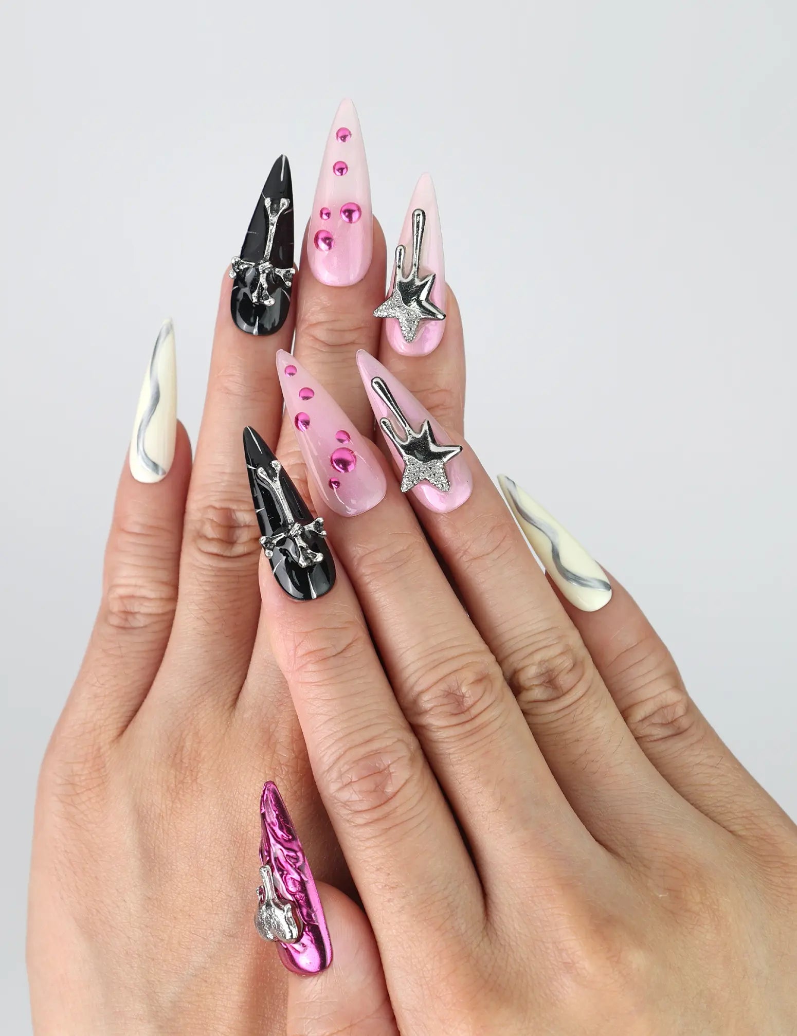Hand model wearing long stiletto press-on nails in black and pink with bold 3D heart and star embellishments
