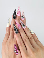 Hand model wearing long stiletto press-on nails in black and pink with bold 3D heart and star embellishments