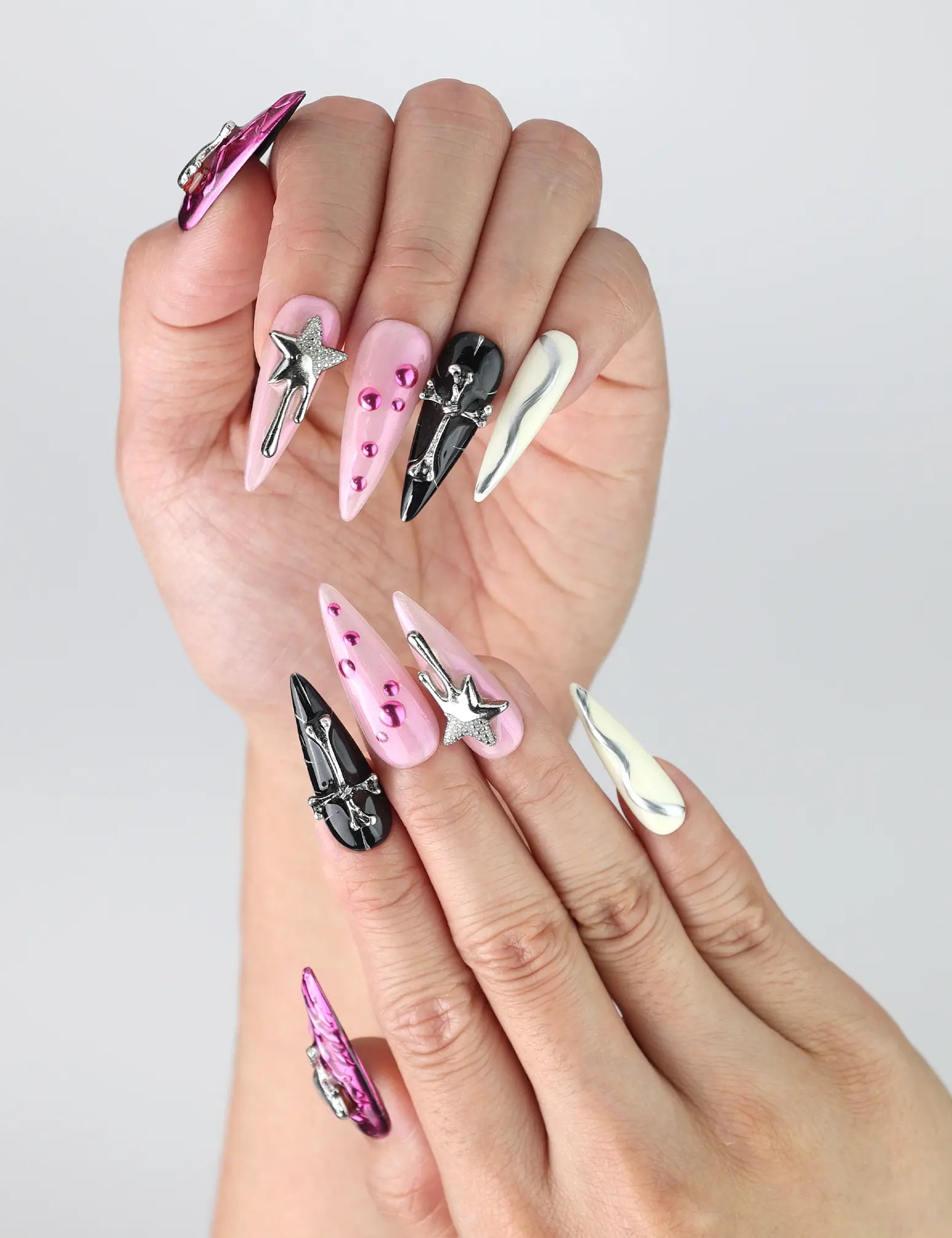 Close-up of Naillover stiletto-shaped nails featuring shiny pink and black base with detailed 3D charms and cosmic accents