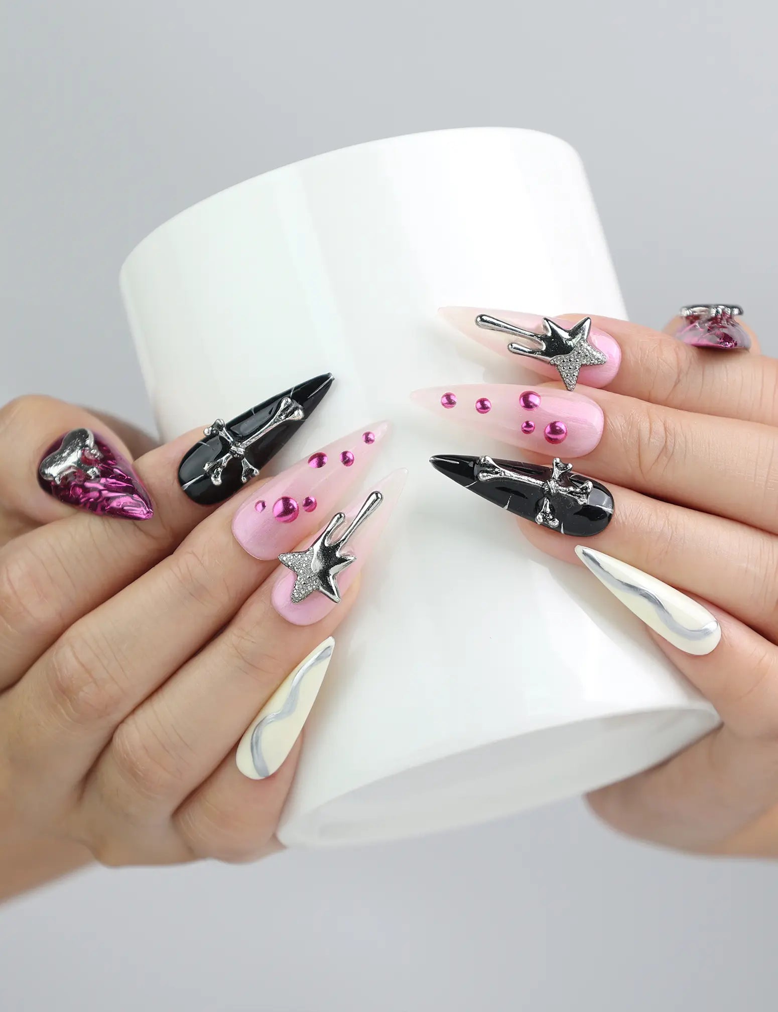 Hand holding a cup, showcasing Naillover’s stiletto press-on nails in pink and black with dramatic 3D charm details