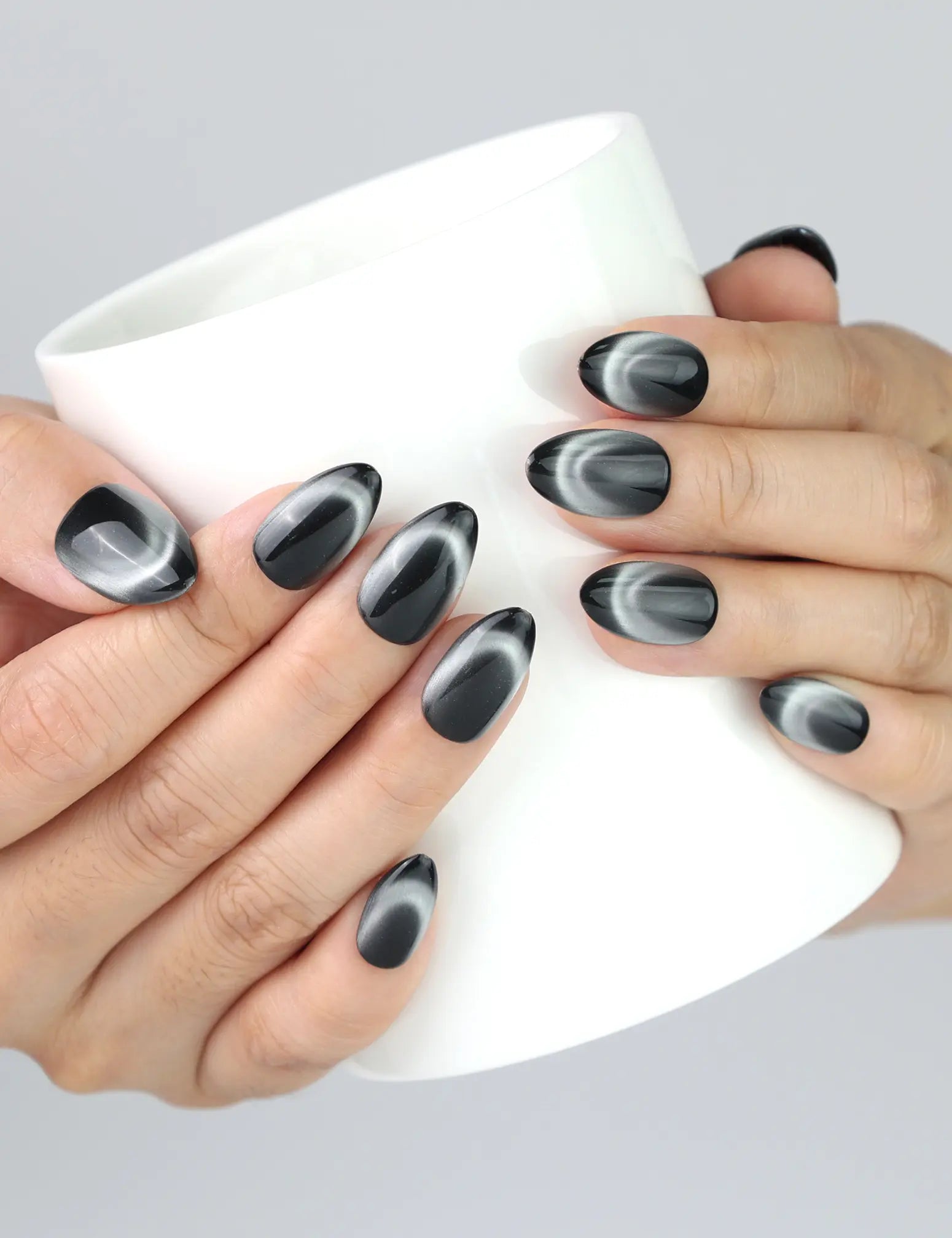 Hand holding a cup while wearing Midnight Gaze black almond nails, cat eye press ons from Naillover Singapore.