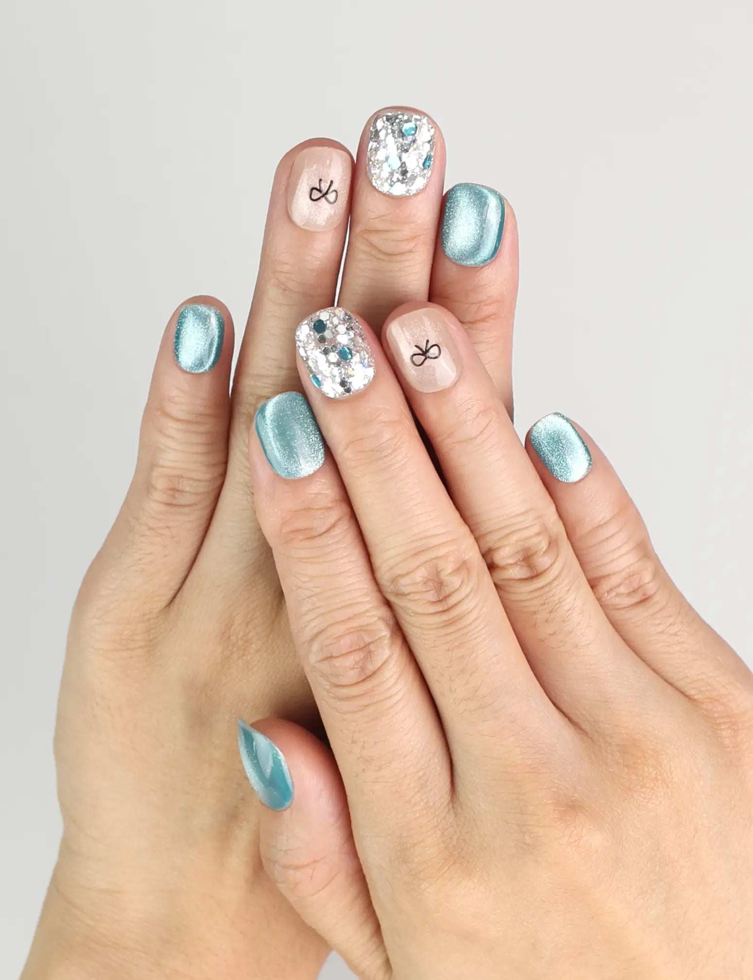 Hand wearing Mint Frost blue shimmer handmade press on nails with crystal accents and bow, naillover Singapore
