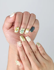 Close-up of Naillover’s handmade square nails featuring soft mint-white tones with sculpted floral art and metallic accents