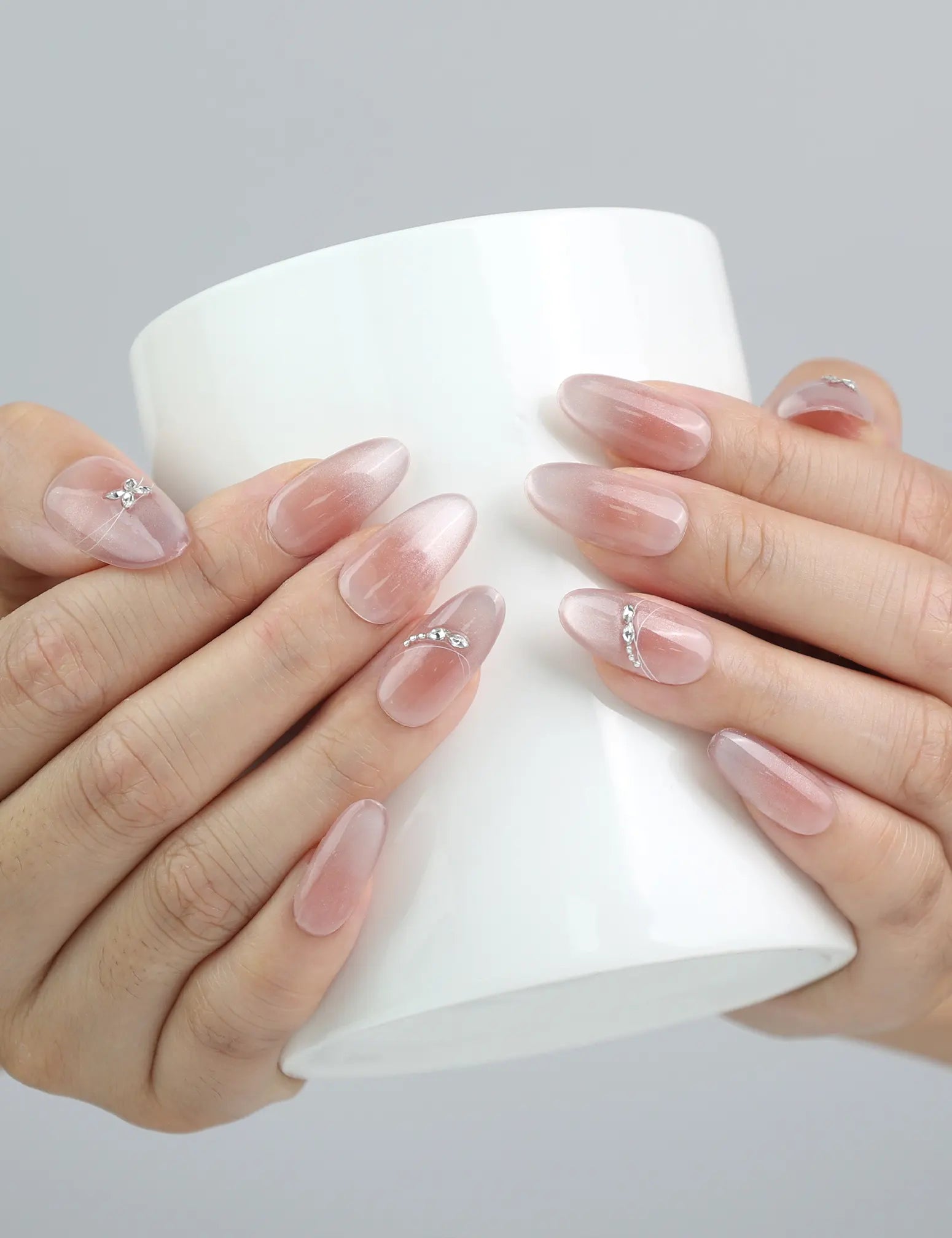 Hand holding a cup, showcasing Naillover’s elegant silver floral nails with pearly shimmer in oval shape