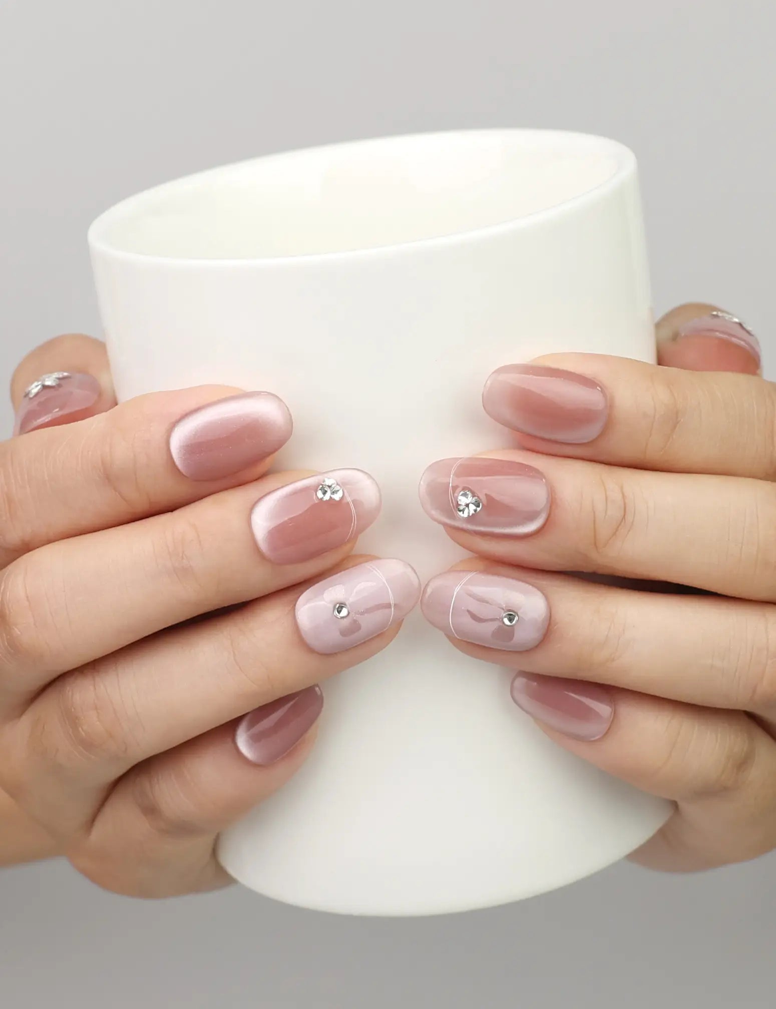 Hand holding a cup while wearing Naillover Misty Rose handmade press on nails with shimmering cat eye nails design.