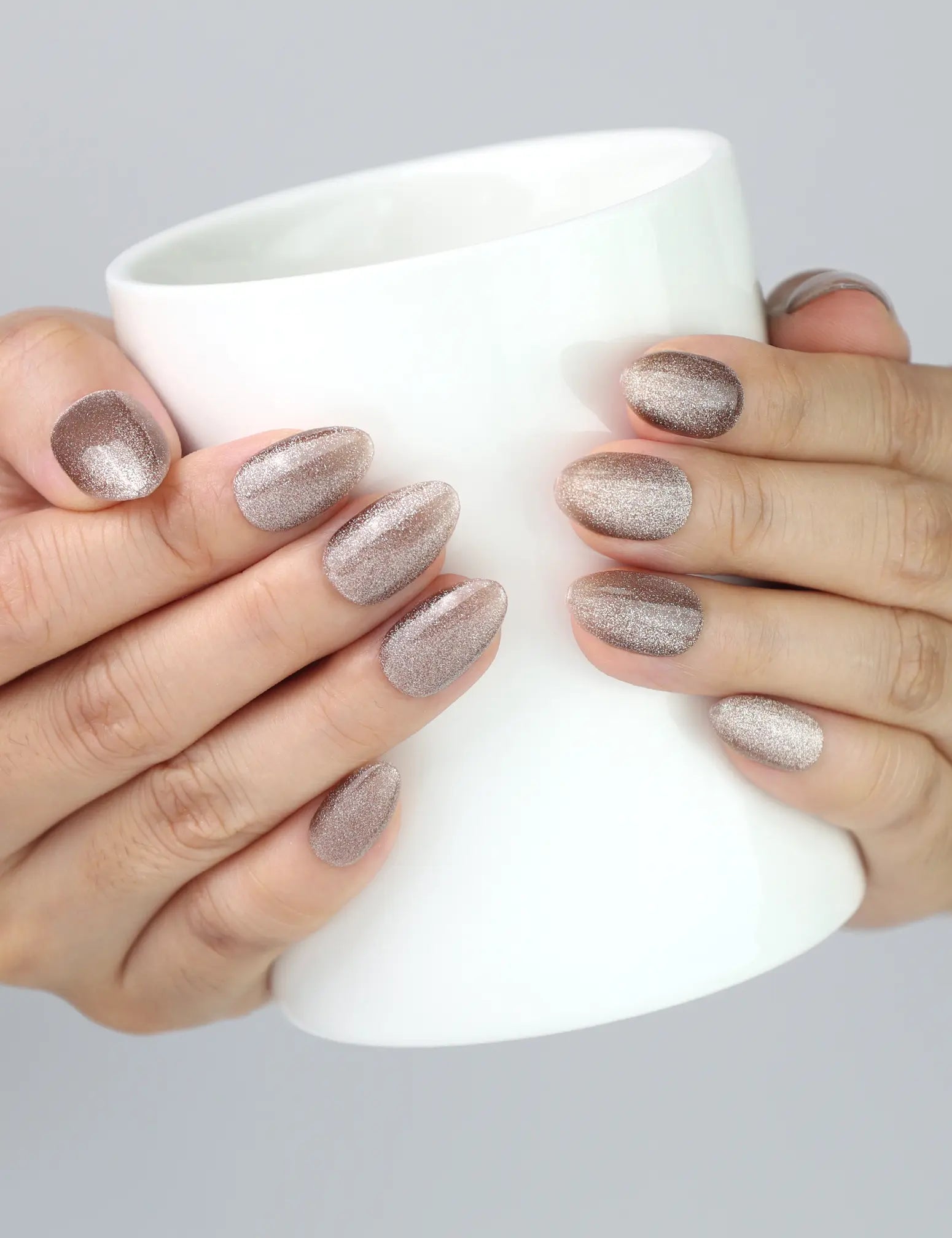 Hand holding a ceramic mug while wearing Mocha Gleam cat eye nails from Naillover, perfect everyday elegance.