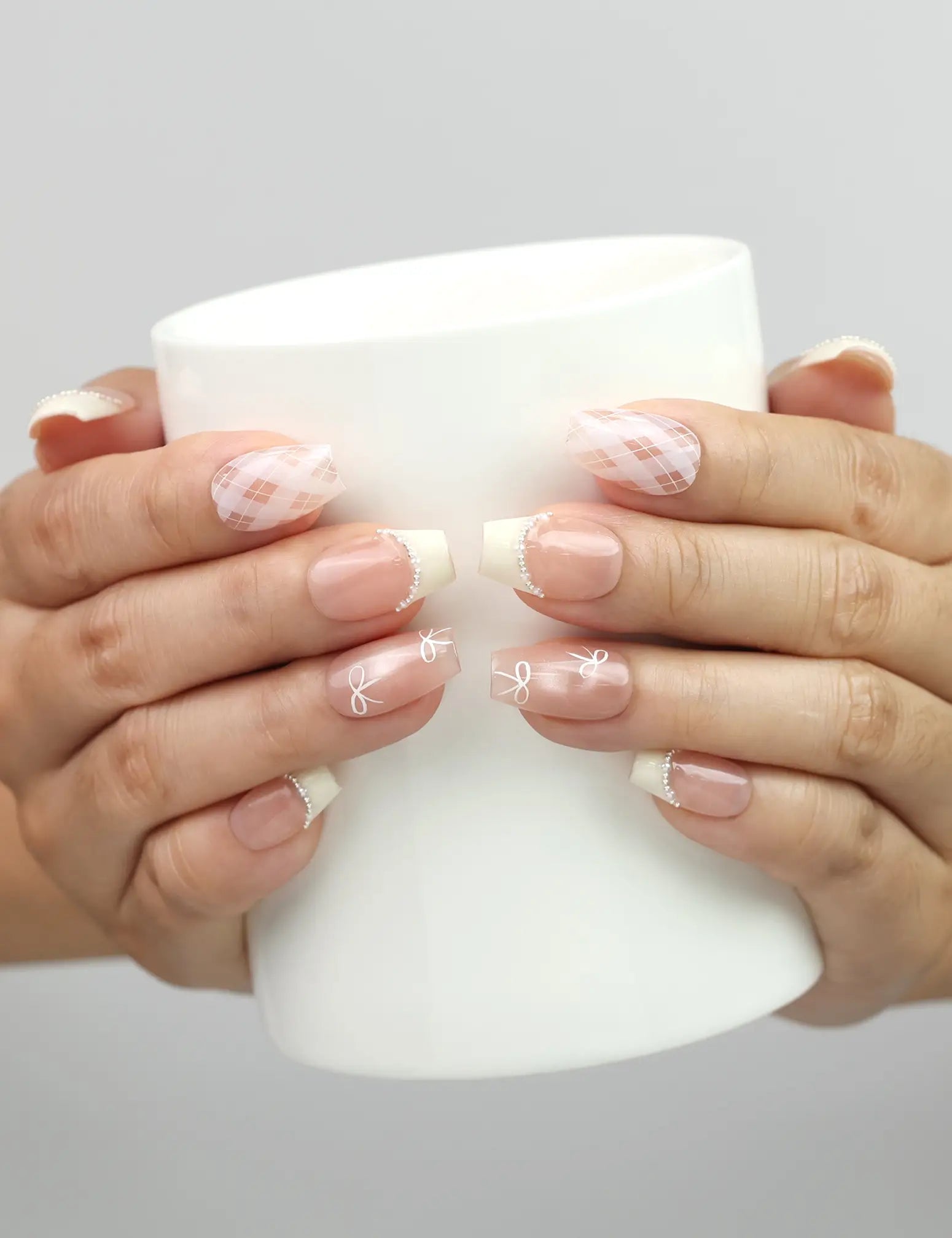 Model holding a cup while wearing Naillover Ballet Bow handmade Singapore press on nails with bows and pearls.