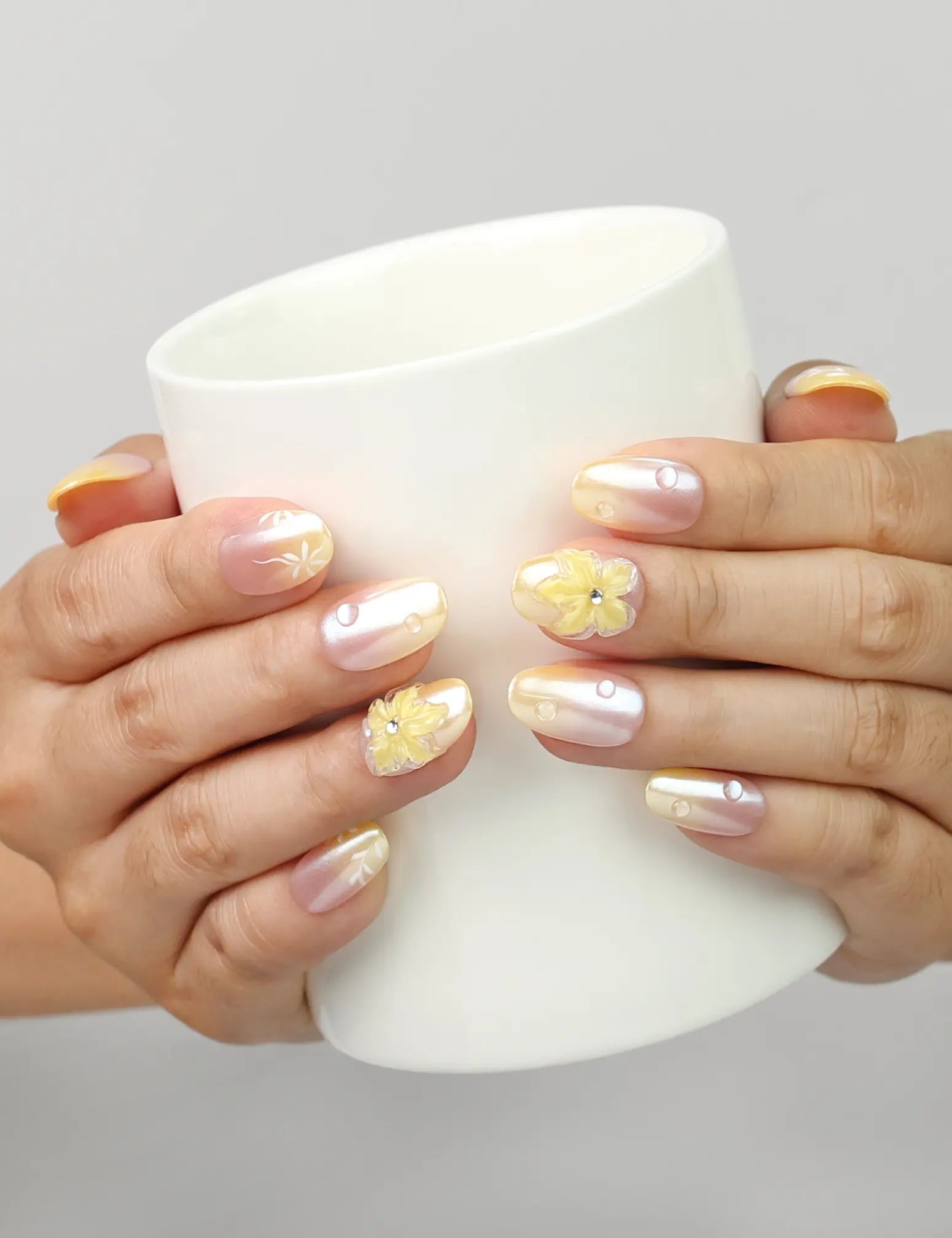 Model holding a cup while wearing Naillover Bloom Whimsy handmade press on nails with peach gradient and 3D flower design.