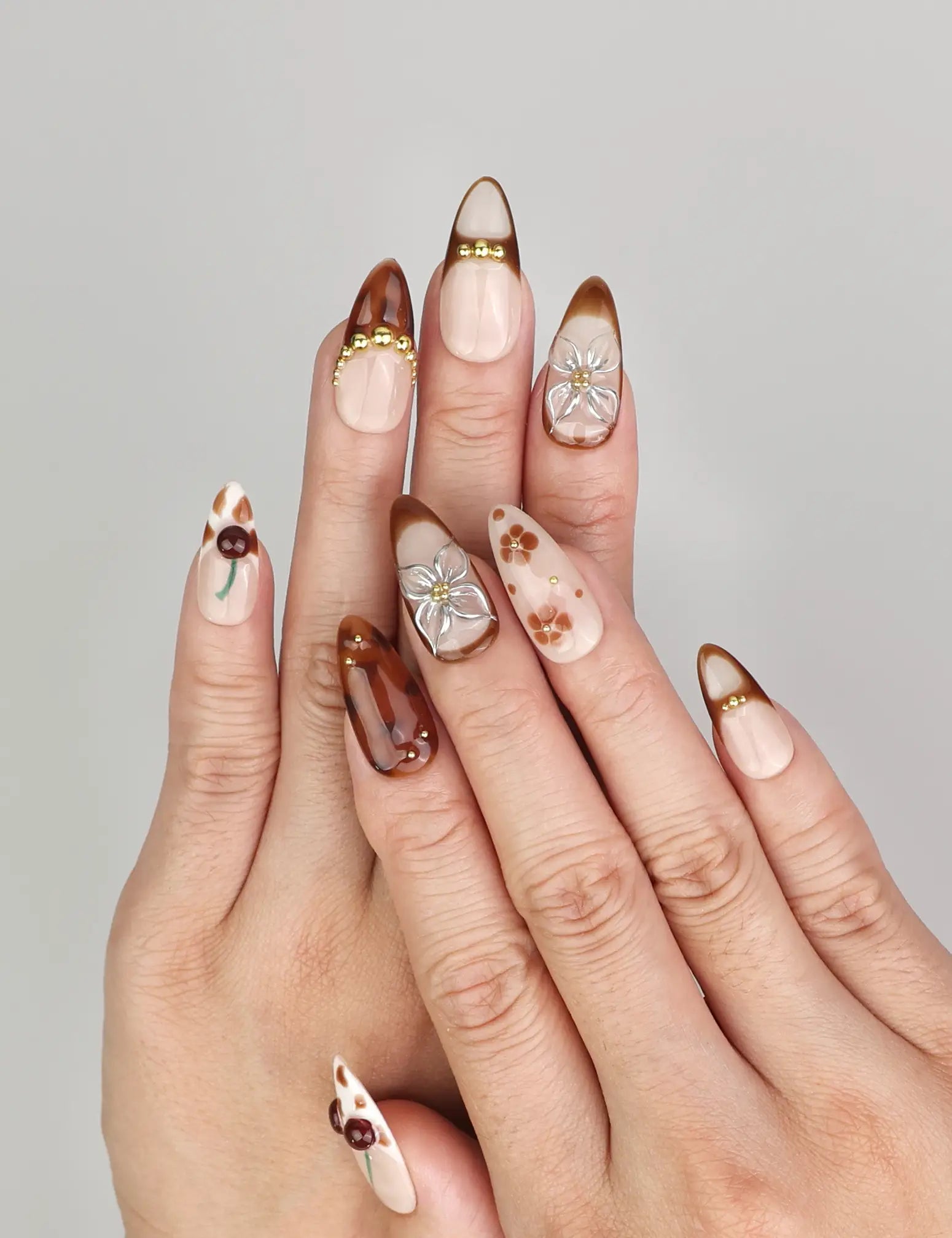 Hand wearing Naillover Blossom Latte Singapore press on nails with beige base, brown floral patterns, and gold accents
