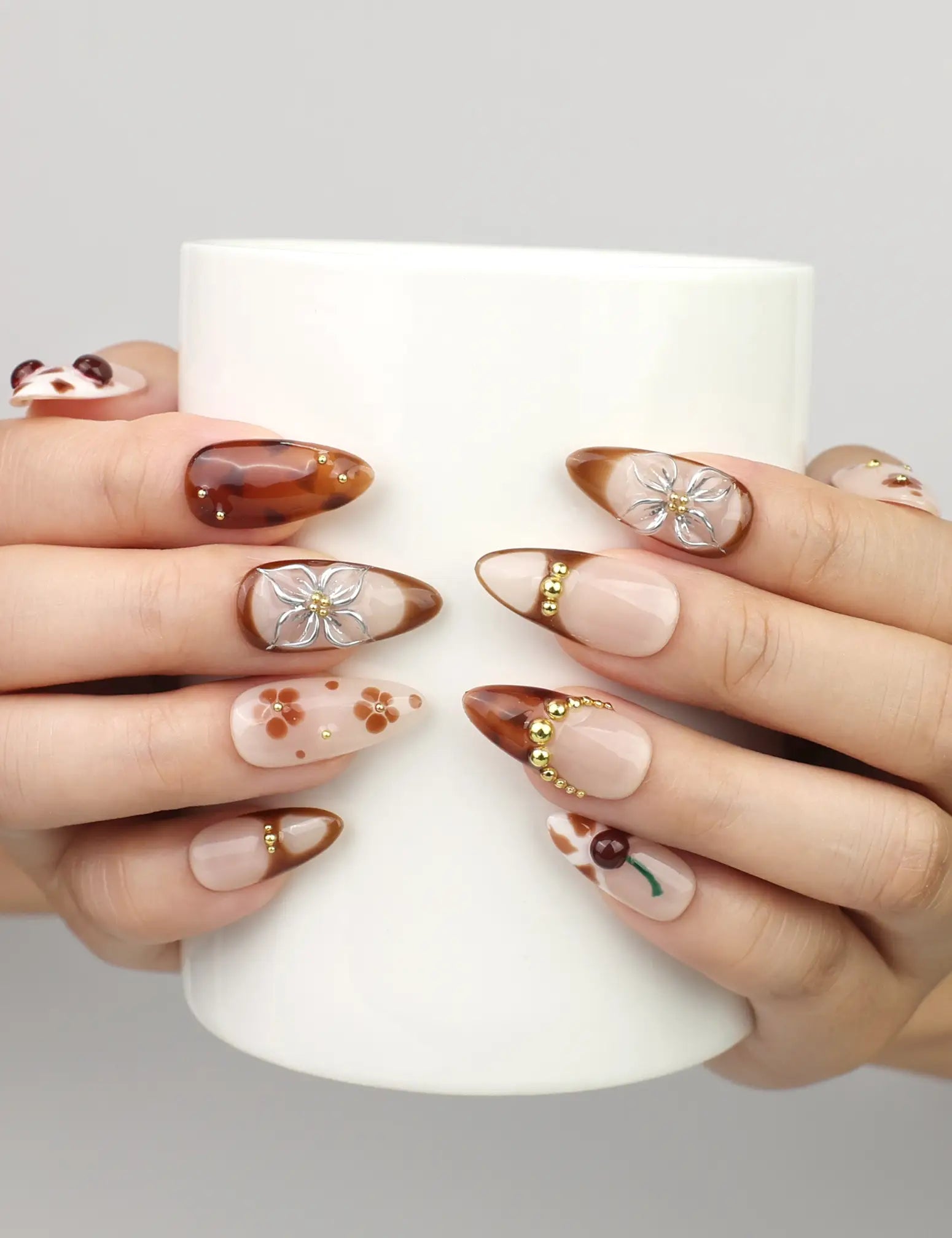 Hand holding a cup while wearing Naillover Blossom Latte Singapore press on nails, showcasing handmade beige nails with floral and gold details