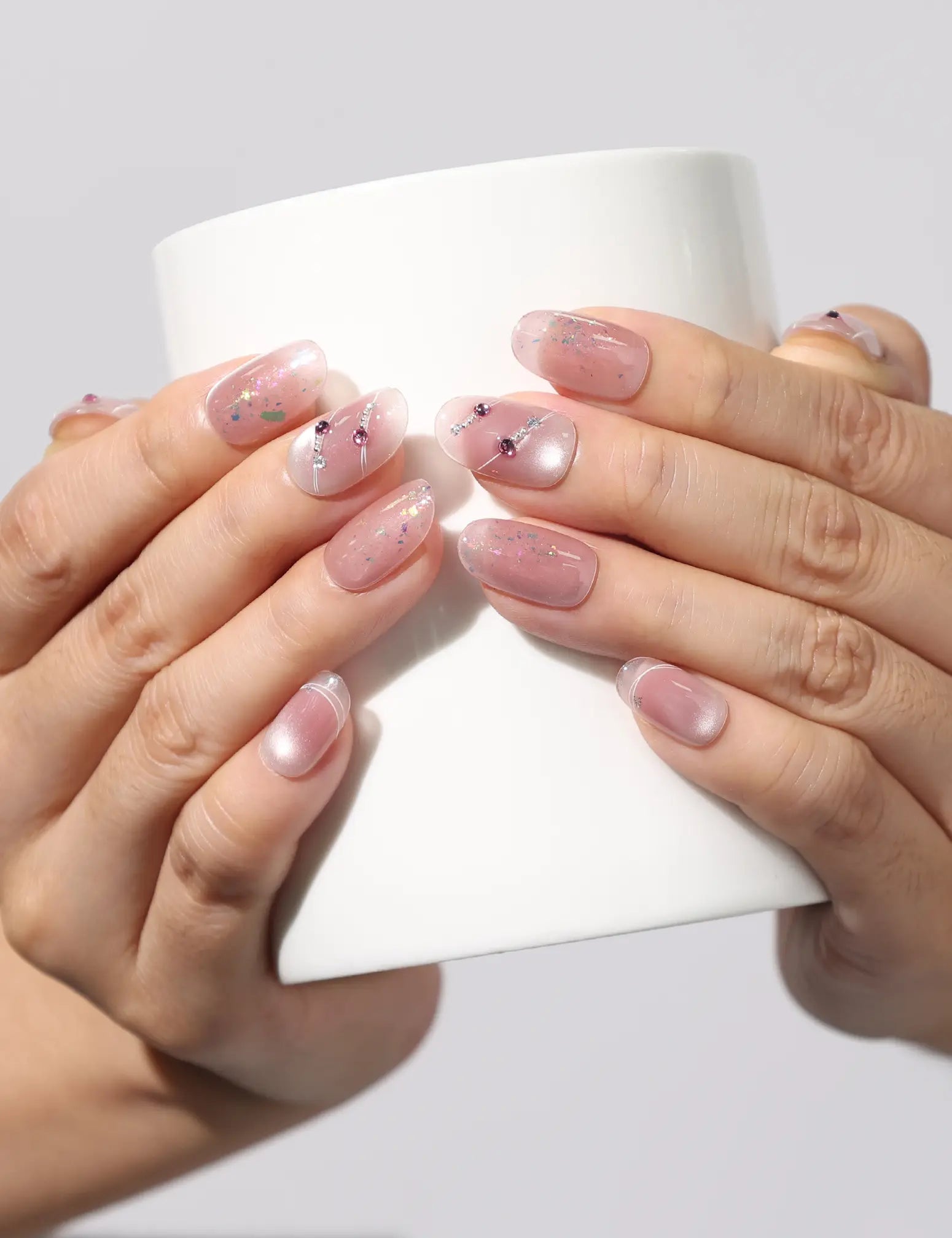 Holding a cup while wearing Blush Diamond Whisper blush pink handmade press on nails with gold and silver glitter by Naillover Singapore.