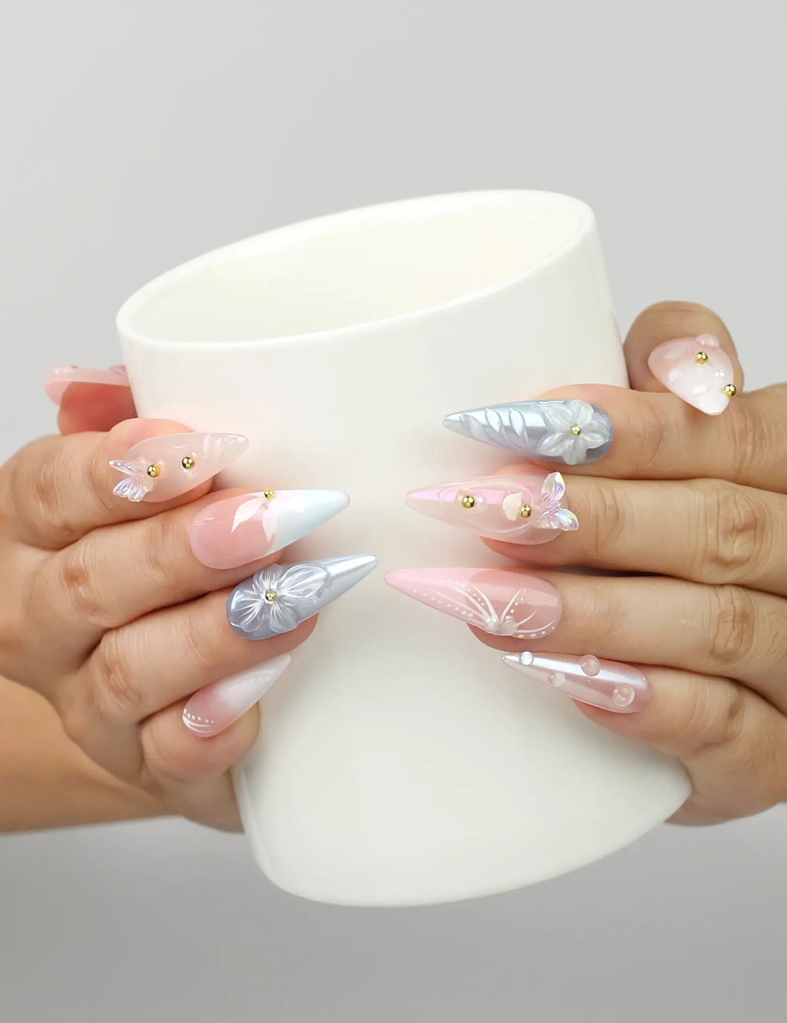 Model holding a cup while wearing Naillover Butterfly's Dream Singapore press on nails with pastel floral motifs.