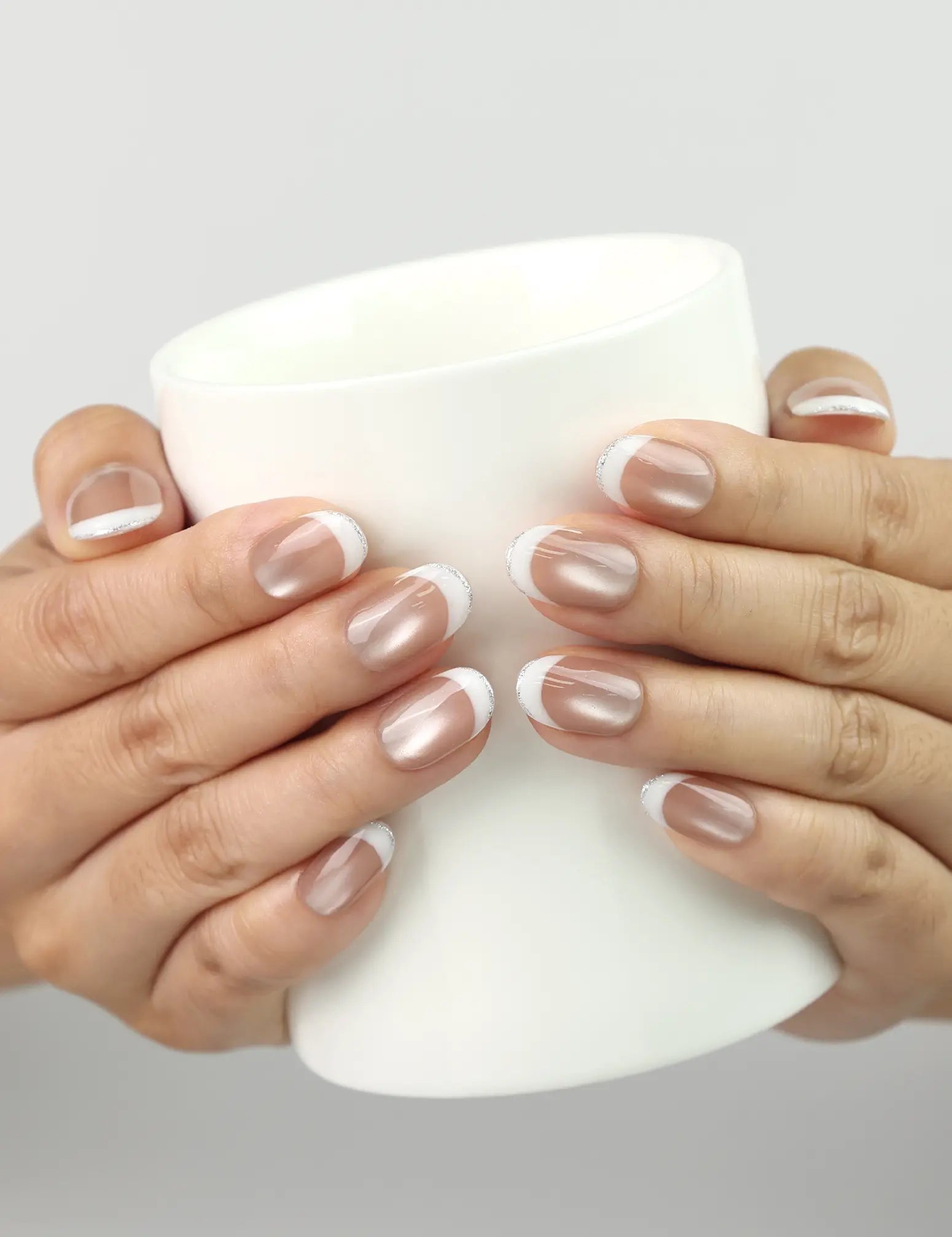 Hand holding a glass while wearing Champagne handmade press on nails, shimmering nude champagne hue, classic nails design by Naillover.