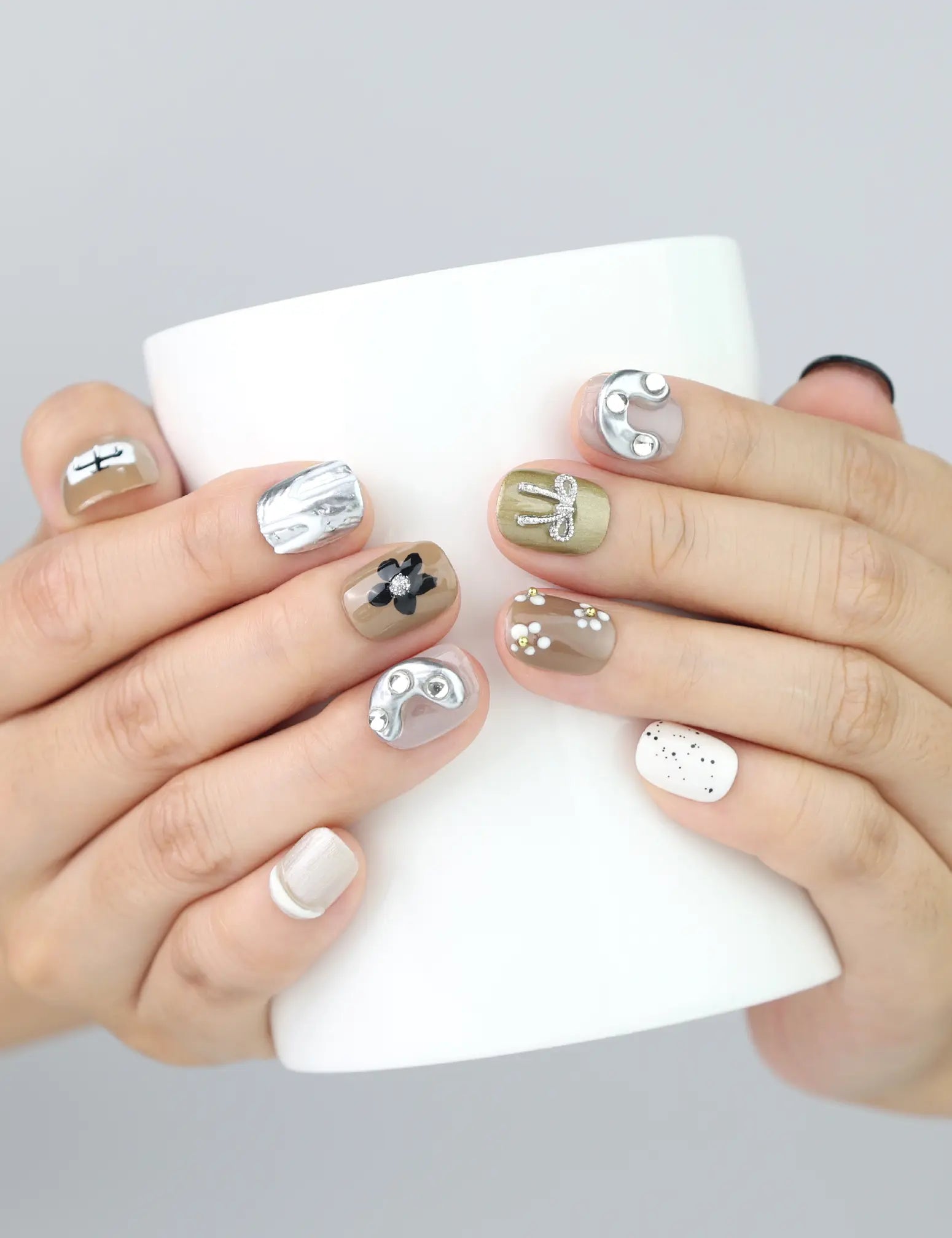 Holding a cup while wearing Chic Doodle press on nails by Naillover, featuring chic neutral palette and handmade bow accents.