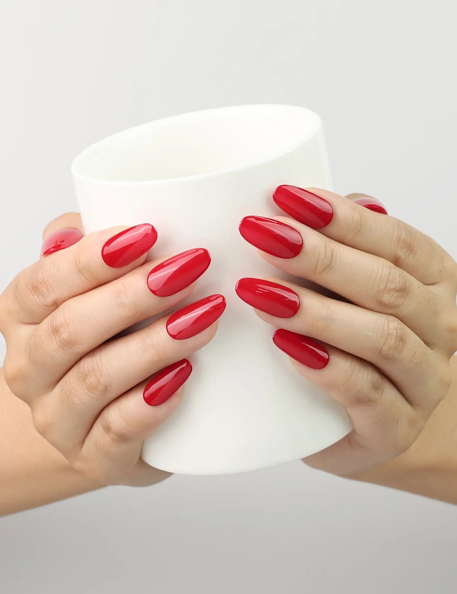 Hand holding a cup with glossy ruby red medium oval handmade Singapore press on nails by Naillover