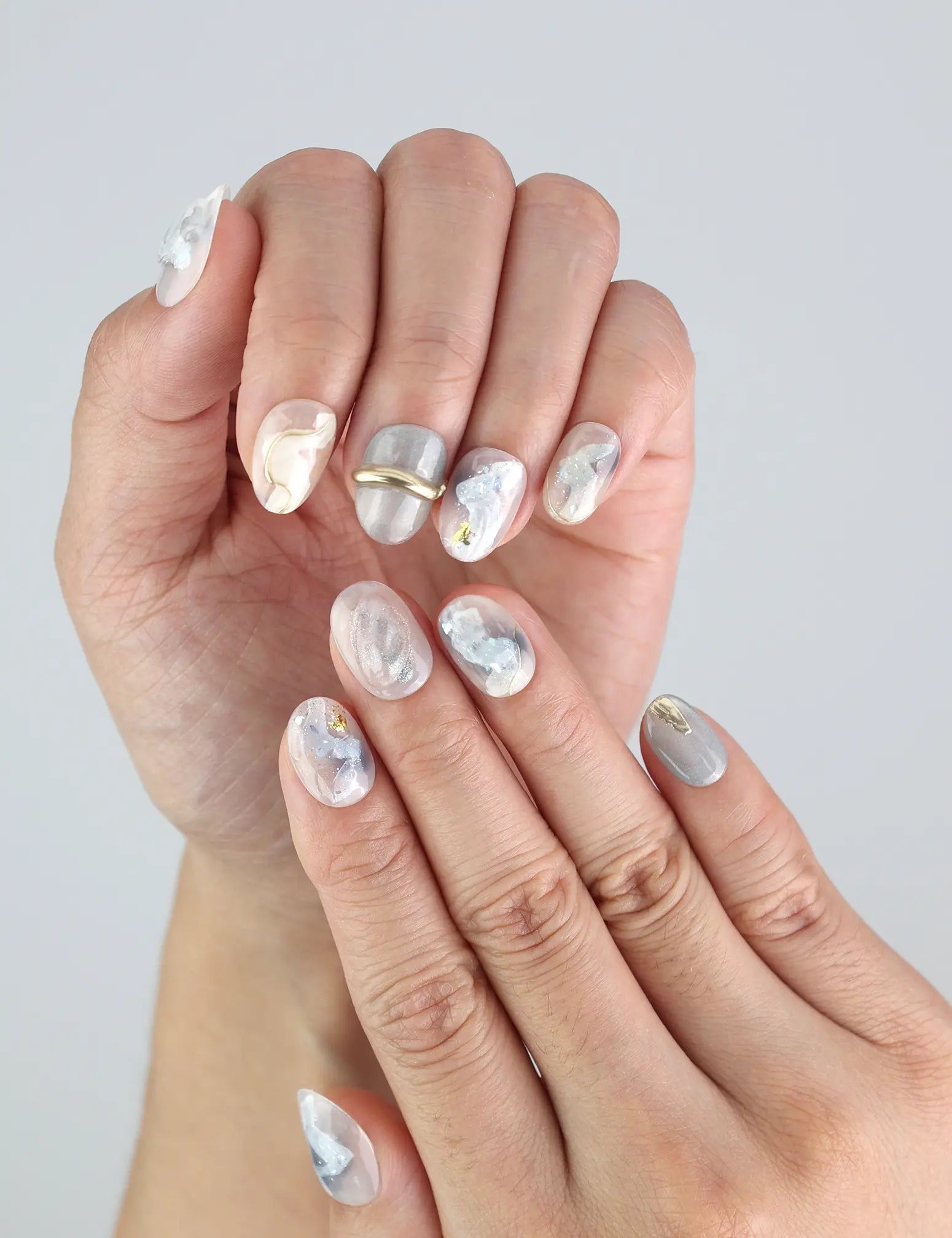 Close-up of Naillover handmade Clear Gleam nails in short square style, featuring white-grey marble and subtle gold shimmer.