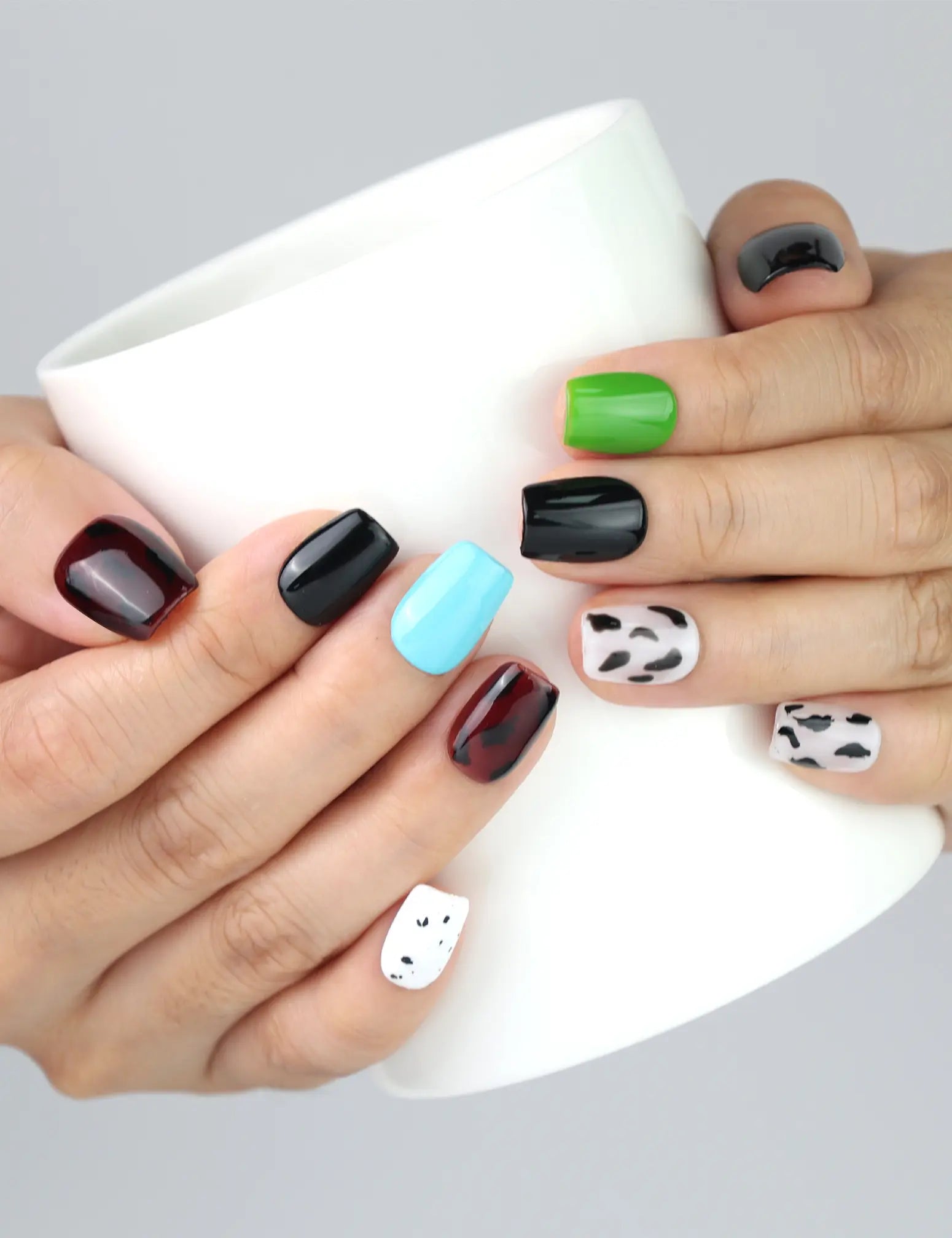 Holding a cup while wearing Cocoa Cow Mix short coffin brown cow print press on nails by Naillover Singapore.