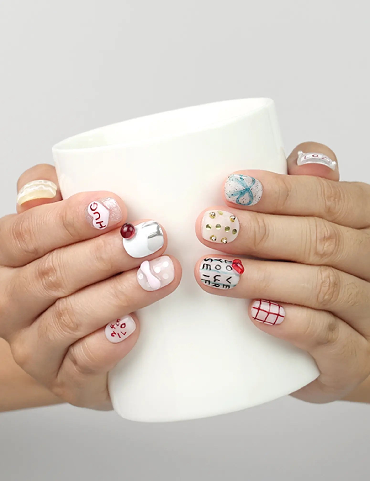 Model holding a cup while wearing Naillover Cozy Hugs handmade Singapore press on nails with bright colors and 3D details.