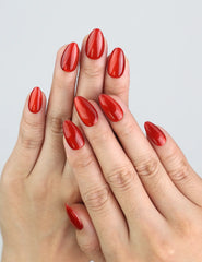 Hand wearing Crimson Magnet red press on nails with magnetic cat-eye effect under studio lighting.