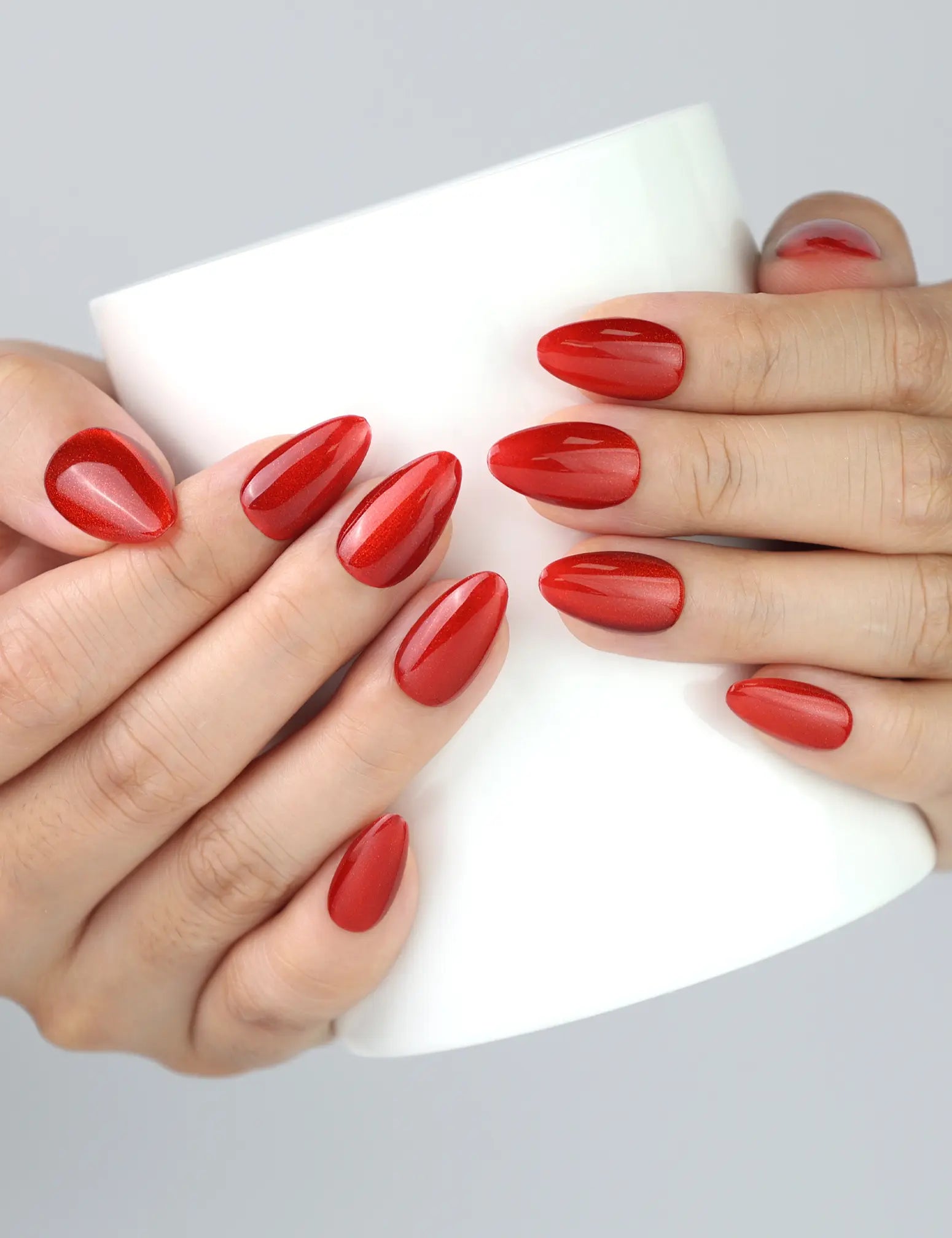 Hand holding coffee cup while wearing Crimson Magnet red cat eye press on nails from Naillover.