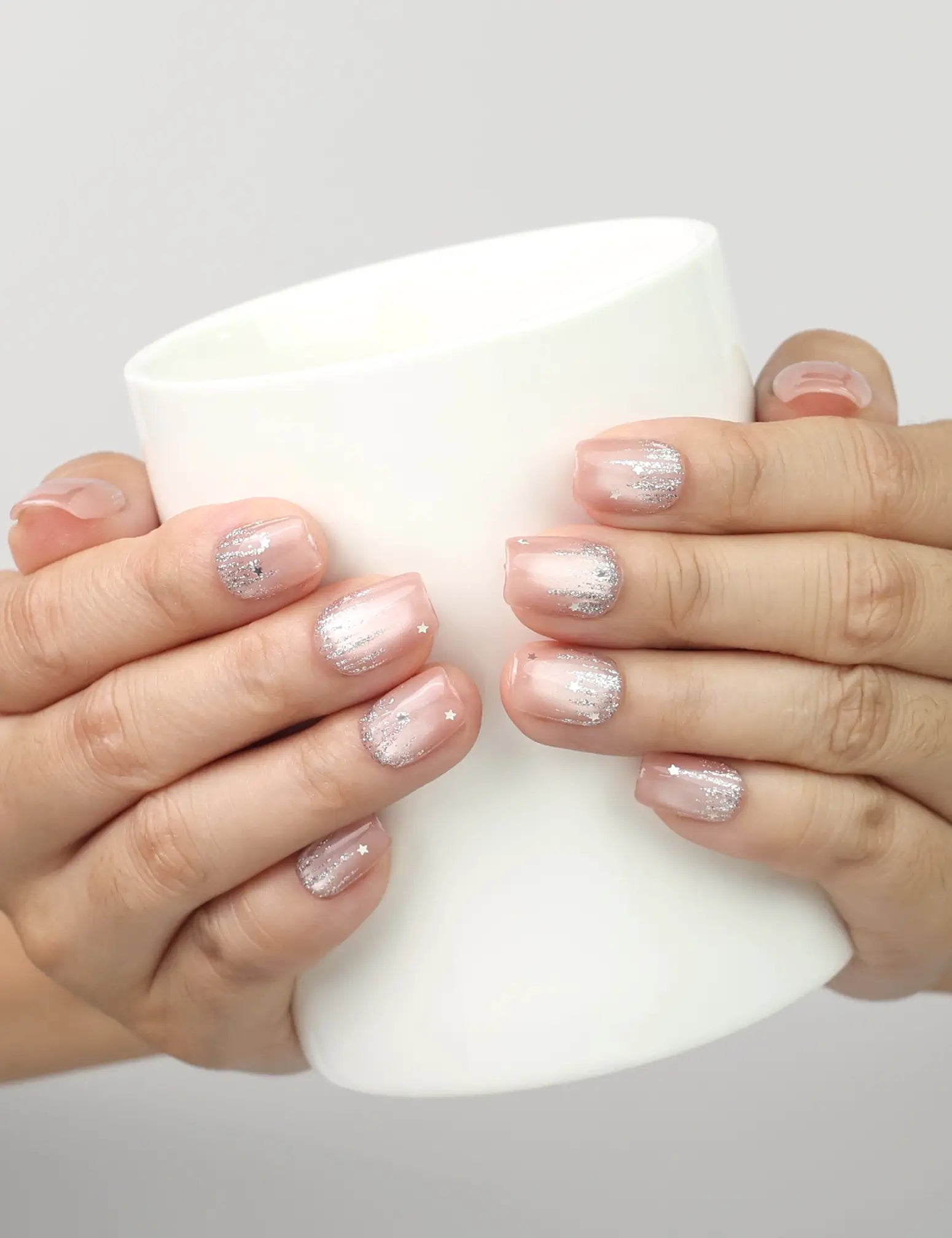Model holding a cup while showing Naillover Crystal Dew cat eye handmade Singapore press on nails with glitter and stars.