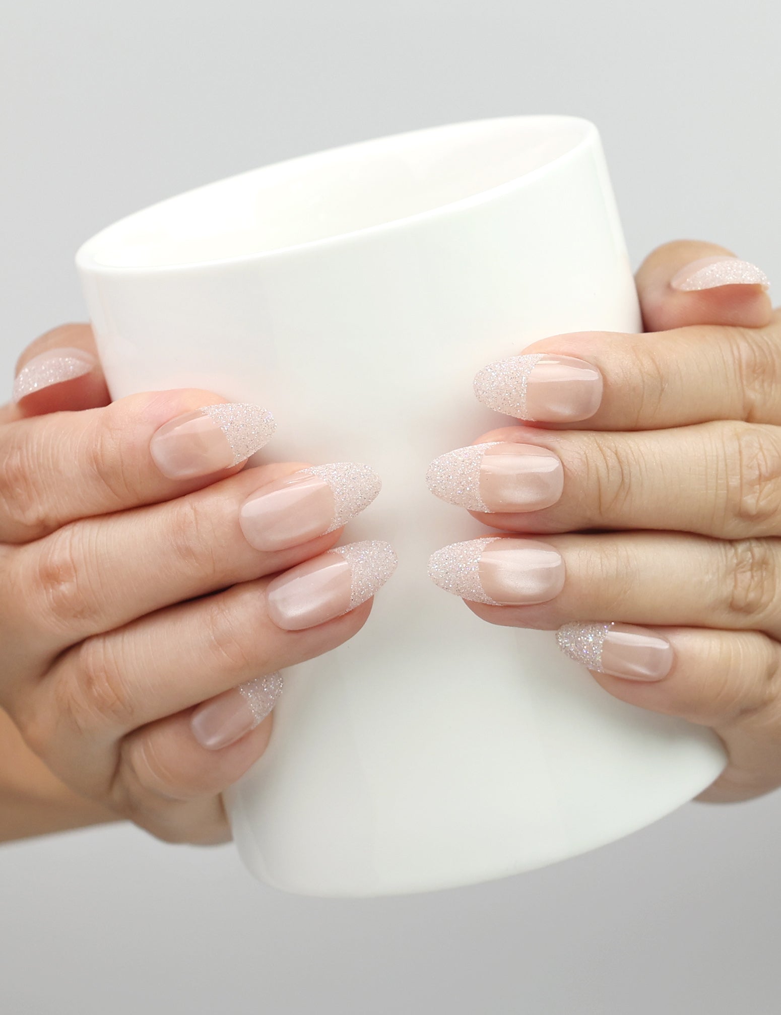 Hand holding a cup while wearing Naillover Crystal Whisper Singapore press on nails with soft nude gradient and subtle crystal accents