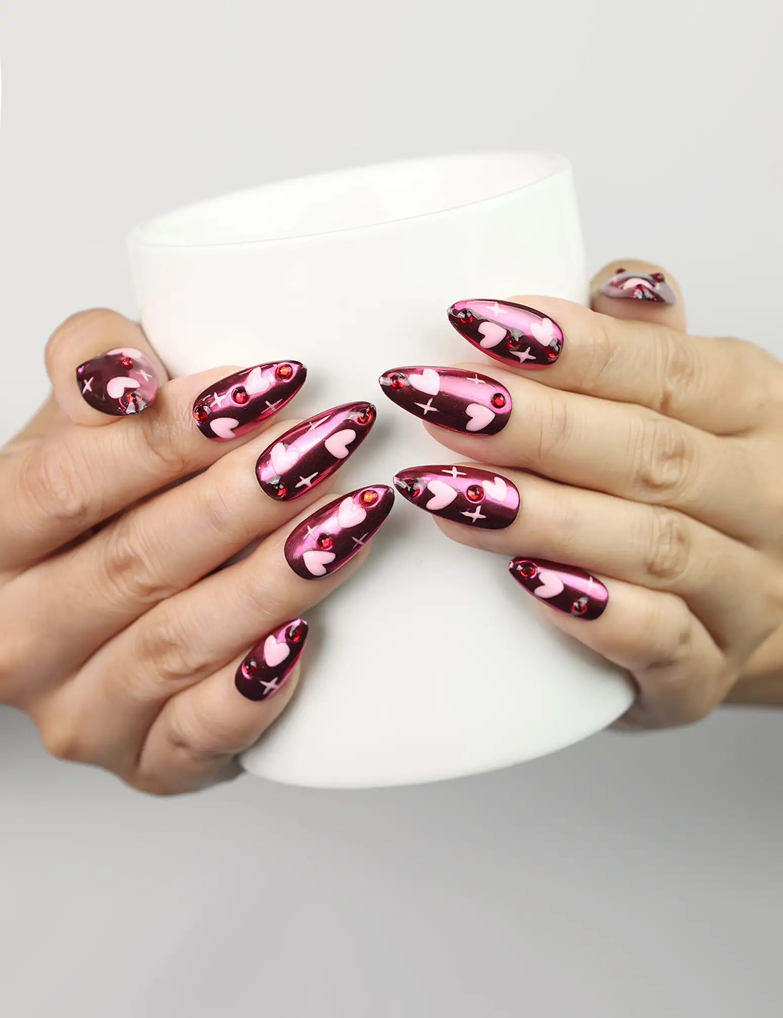 Cupid's Curve Singapore press on nails by Naillover in magenta with heart designs and rhinestones, shown holding a coffee cup