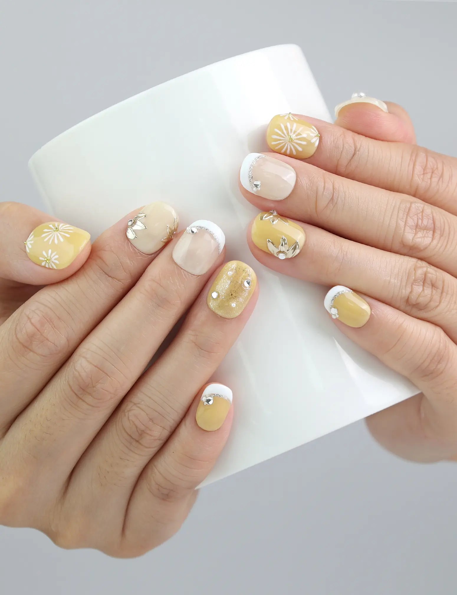 Hand holding a cup while wearing Daisy Glow press on nails, blending floral elegance with effortless daily style.