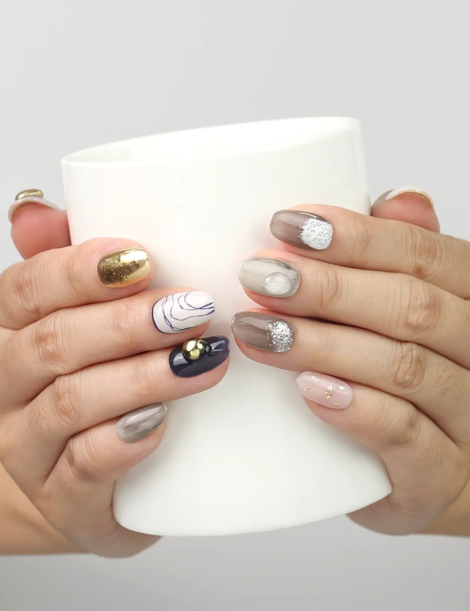Model holding a cup while wearing Naillover Eclipse Core handmade Singapore press on nails with chic marbled patterns.
