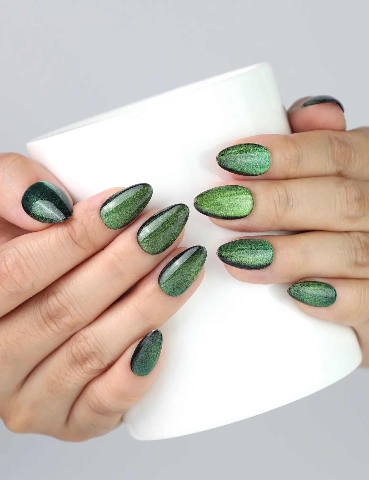 Holding a cup while wearing Emerald Optic green cat eye press on nails by Naillover.