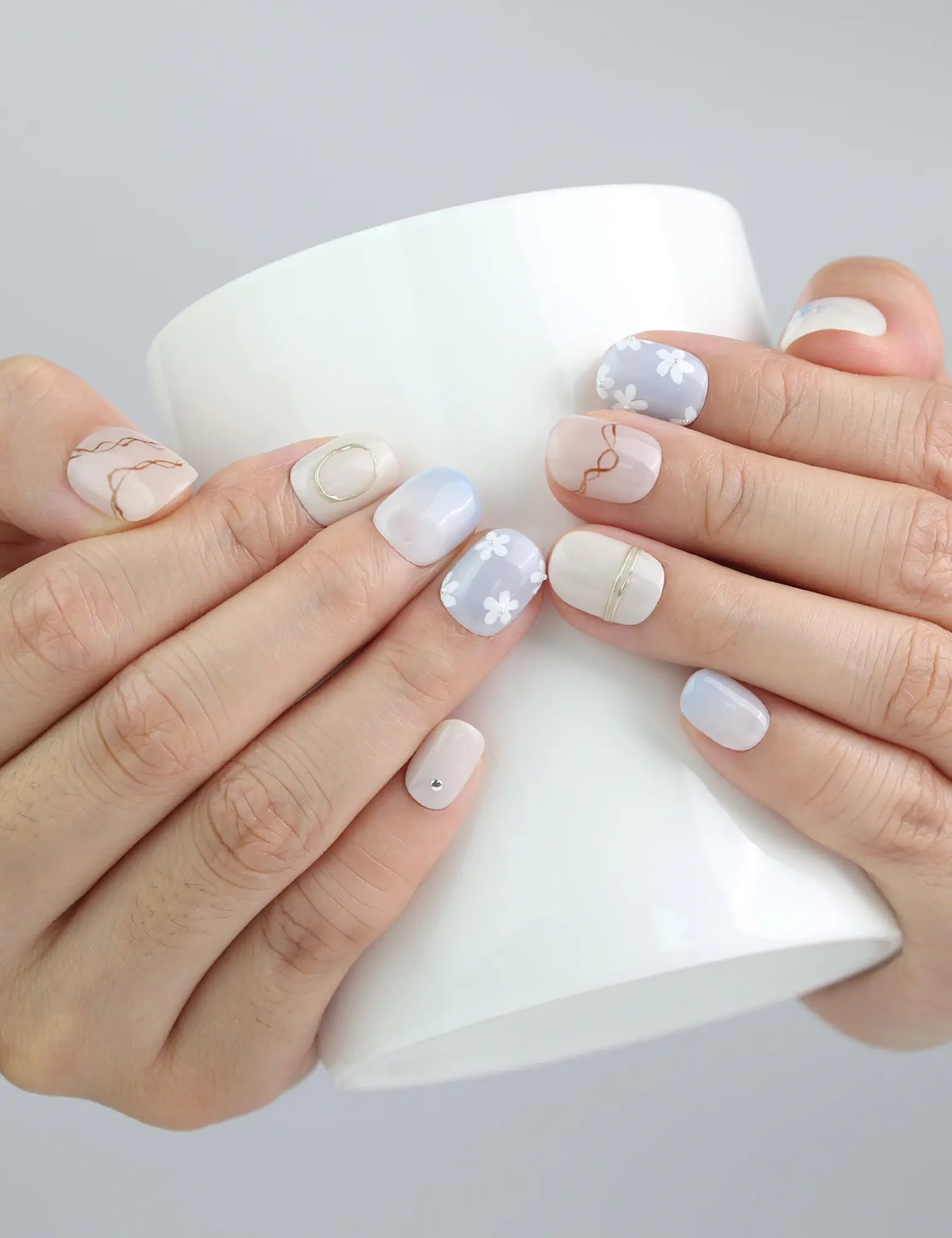 Holding a coffee cup while wearing Naillover Gentle Echo nails, showcasing refined pastel nails with flower accents.
