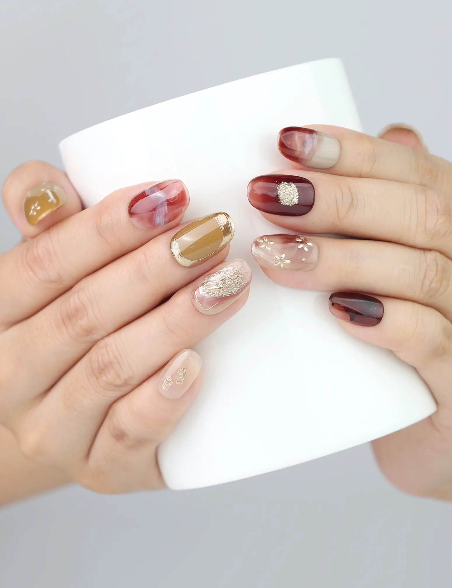 Naillover Gilded Brown handmade press on nails in cozy lifestyle shot—burgundy flowers and golden shimmer while holding a cup.