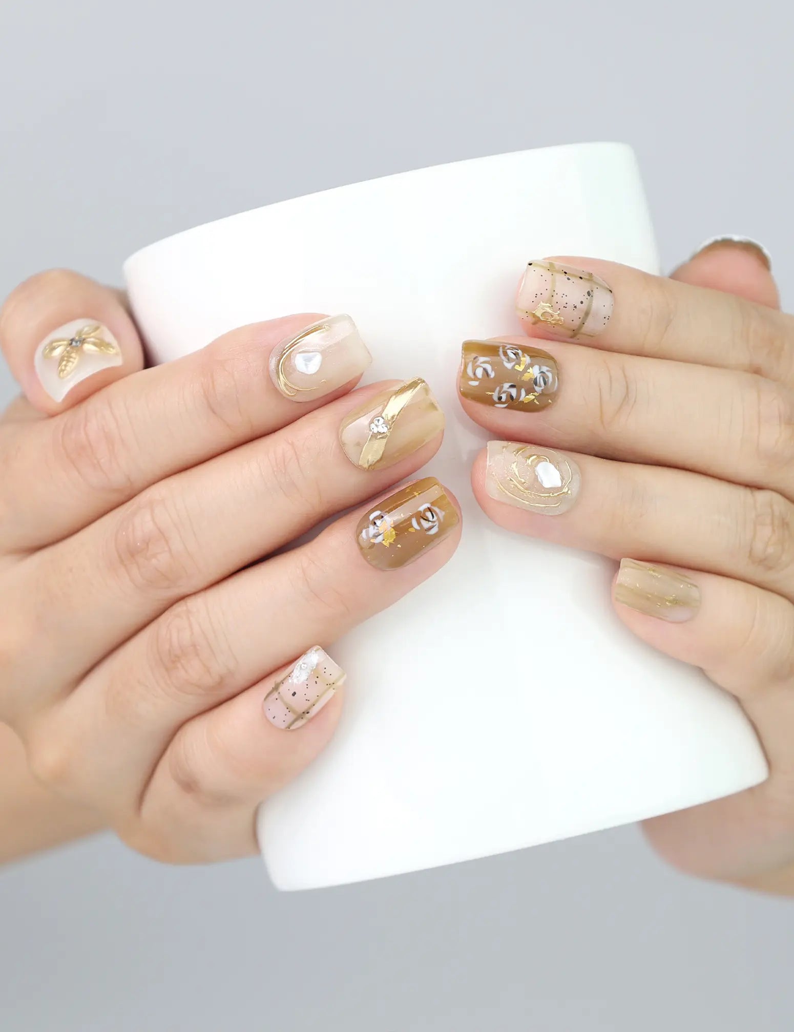 Lifestyle shot of Naillover Gilded Grace 3D handmade press on nails while holding a ceramic cup—soft beige and floral shimmer.