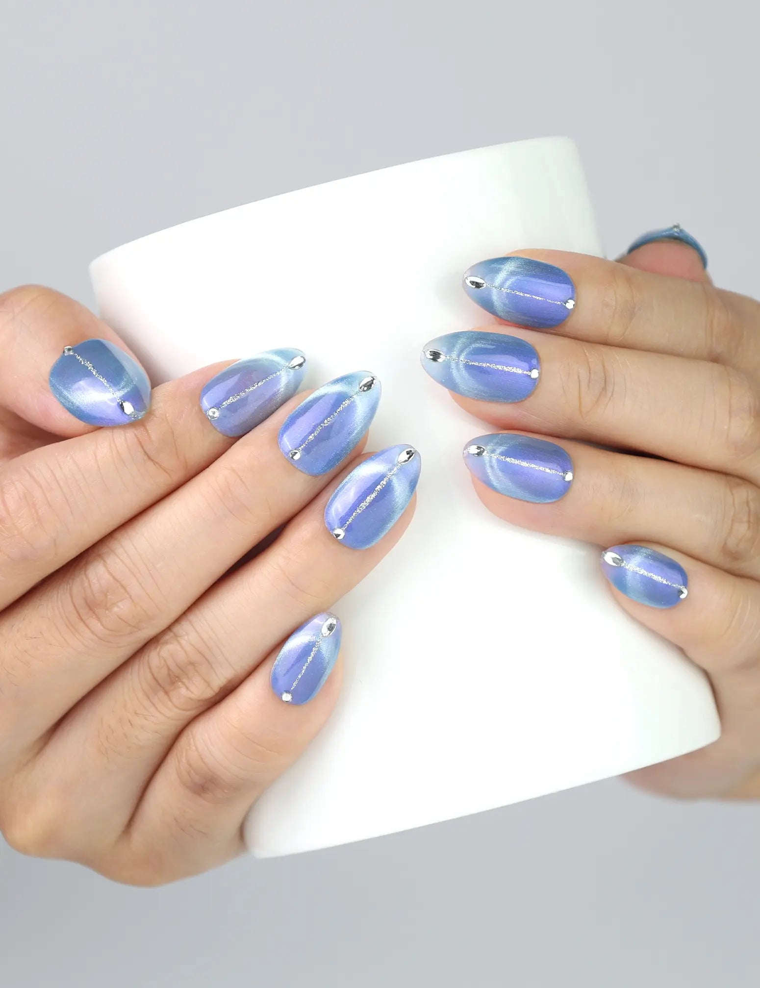 Holding a warm mug while wearing Glacier Veil cat eye press on nails by Naillover.