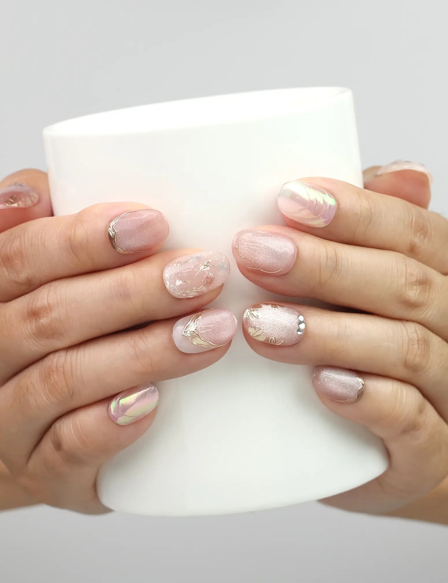 Model holding a cup while wearing Naillover Glimmer Blossom Singapore press on nails with gold leaf and rhinestones.