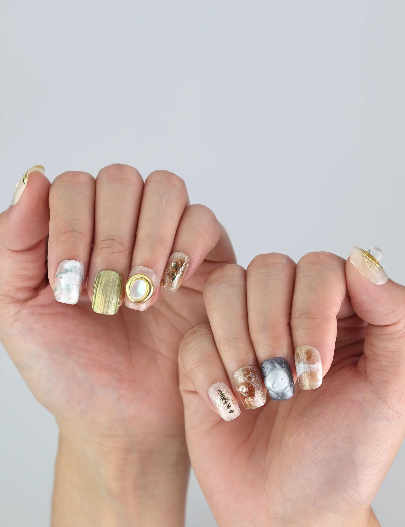 Close-up of Naillover Gold Leaf Whisper nails—floral accents, gold stripes, and 3D pearl for a trendy, classic finish.