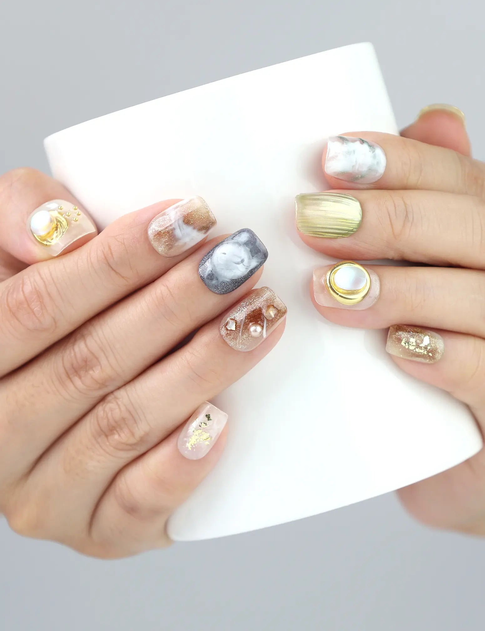 Hand gripping a cup with Gold Leaf Whisper press on nails by Naillover—featuring shimmer gold lines and pearl accents.